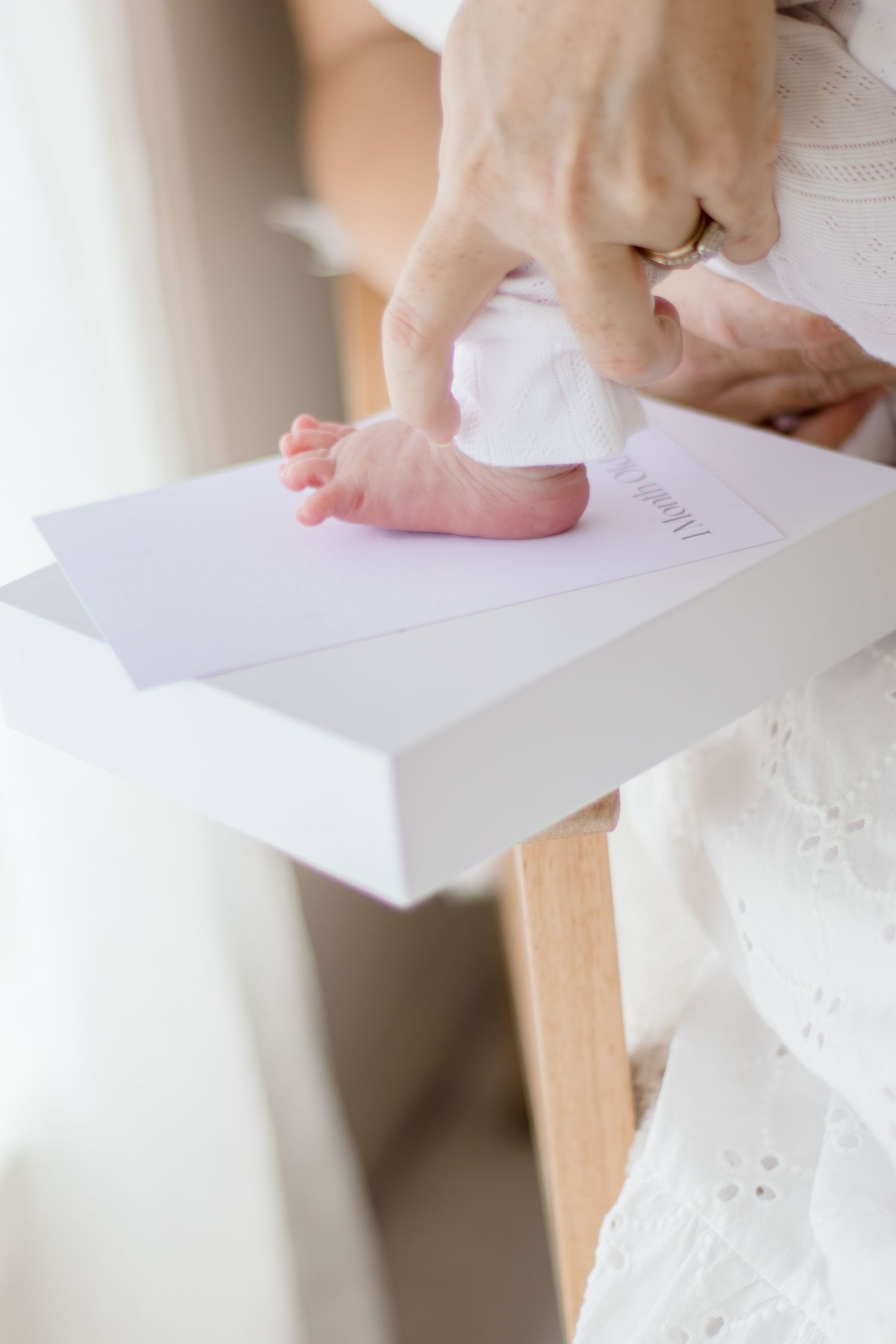 Close-up of a newborn baby's tiny foot resting on a white memory book held by an adult's hands.