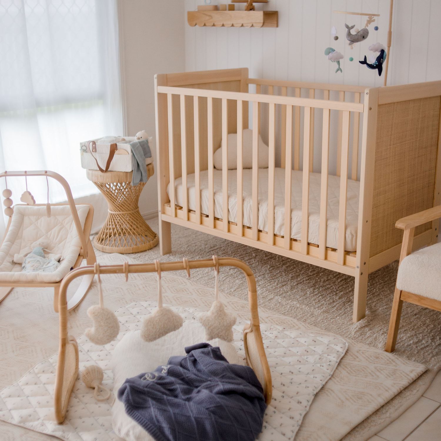 Modern neutral-toned nursery with wooden crib, rattan furniture and play gym on textured rug.