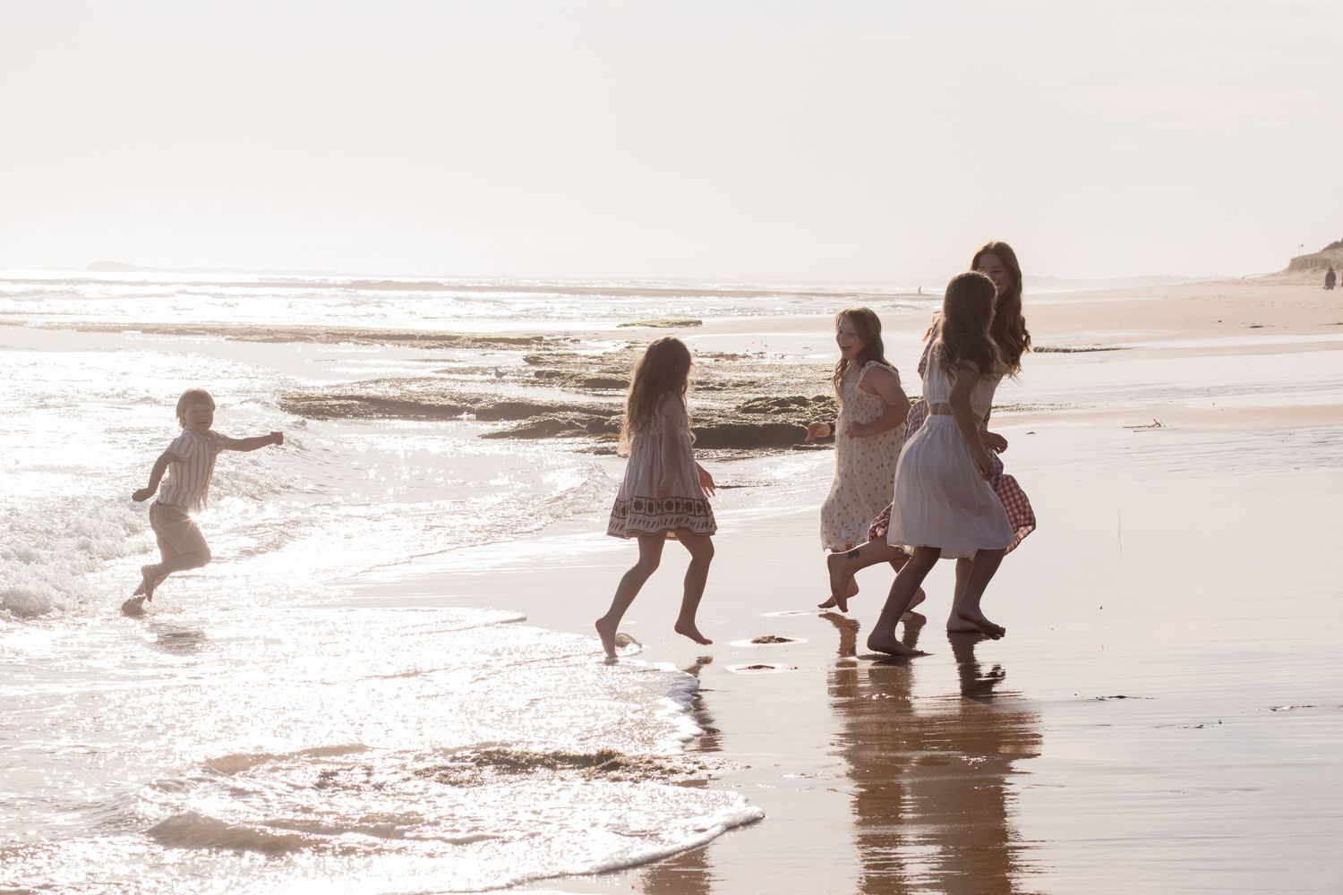 Silhouettes of figures dancing and playing along a beach shoreline at sunset with ocean waves in the background.