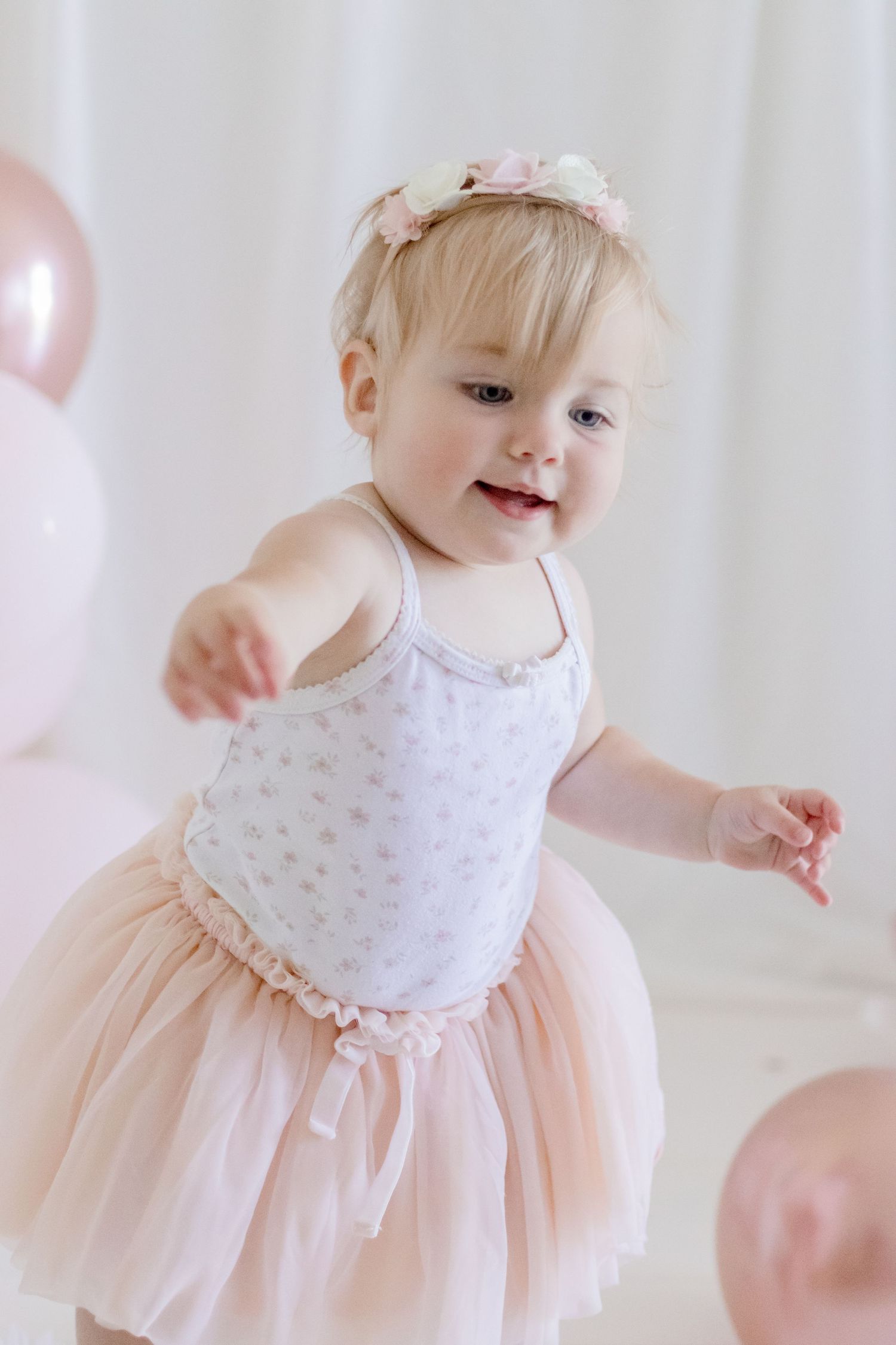 Child in pink tutu dress dancing among balloons in a whimsical photoshoot.