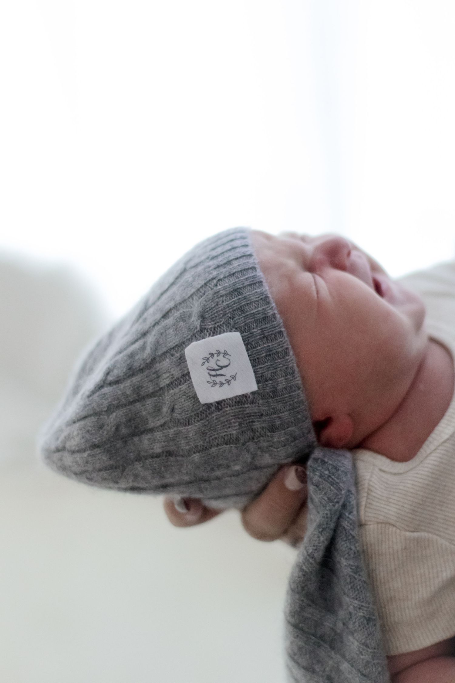 Baby wearing soft gray knit beanie hat with small tag label.