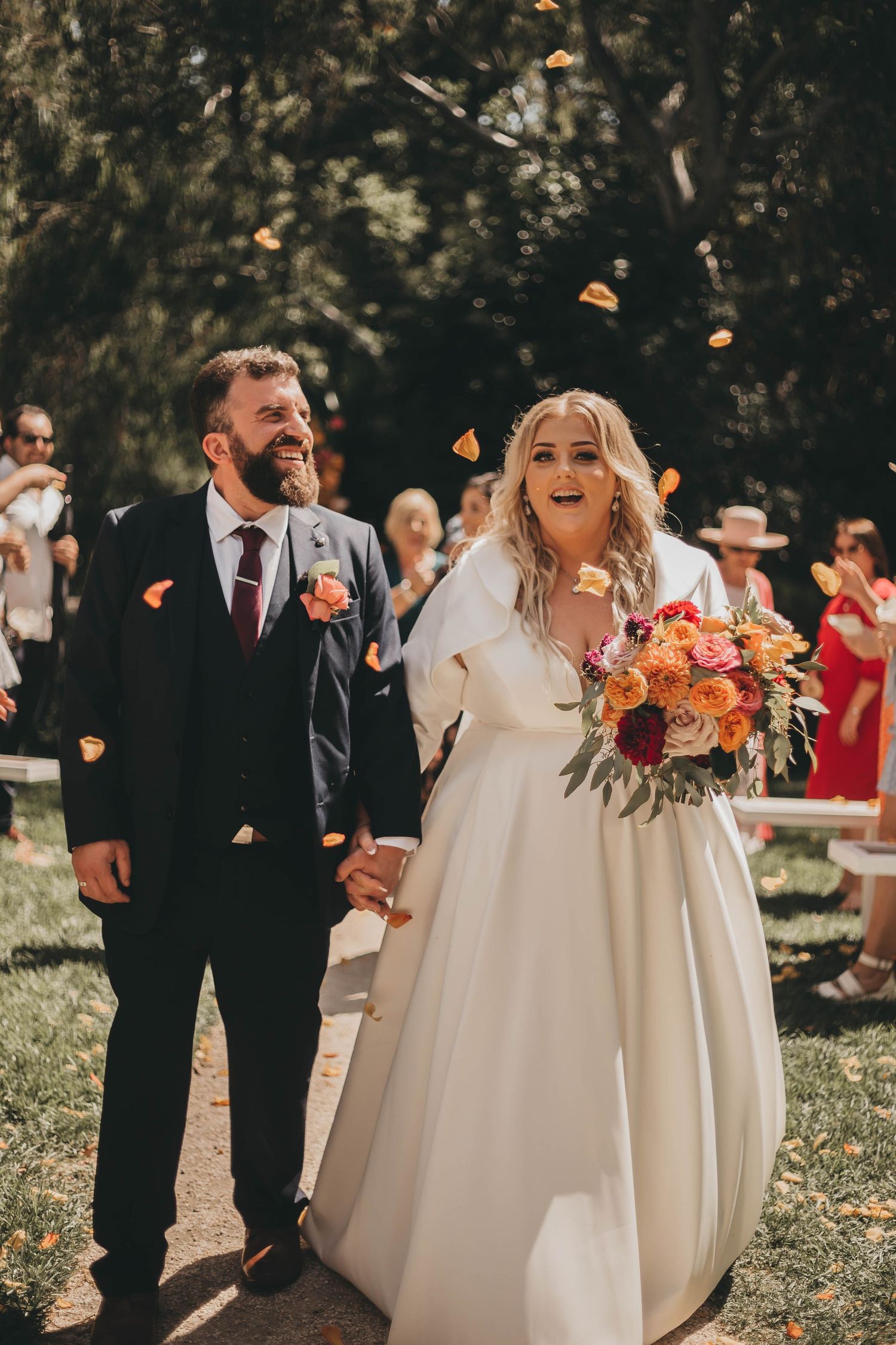 A joyful wedding ceremony outdoors with bridesmaids in white dresses holding colorful autumn bouquets in the garden.