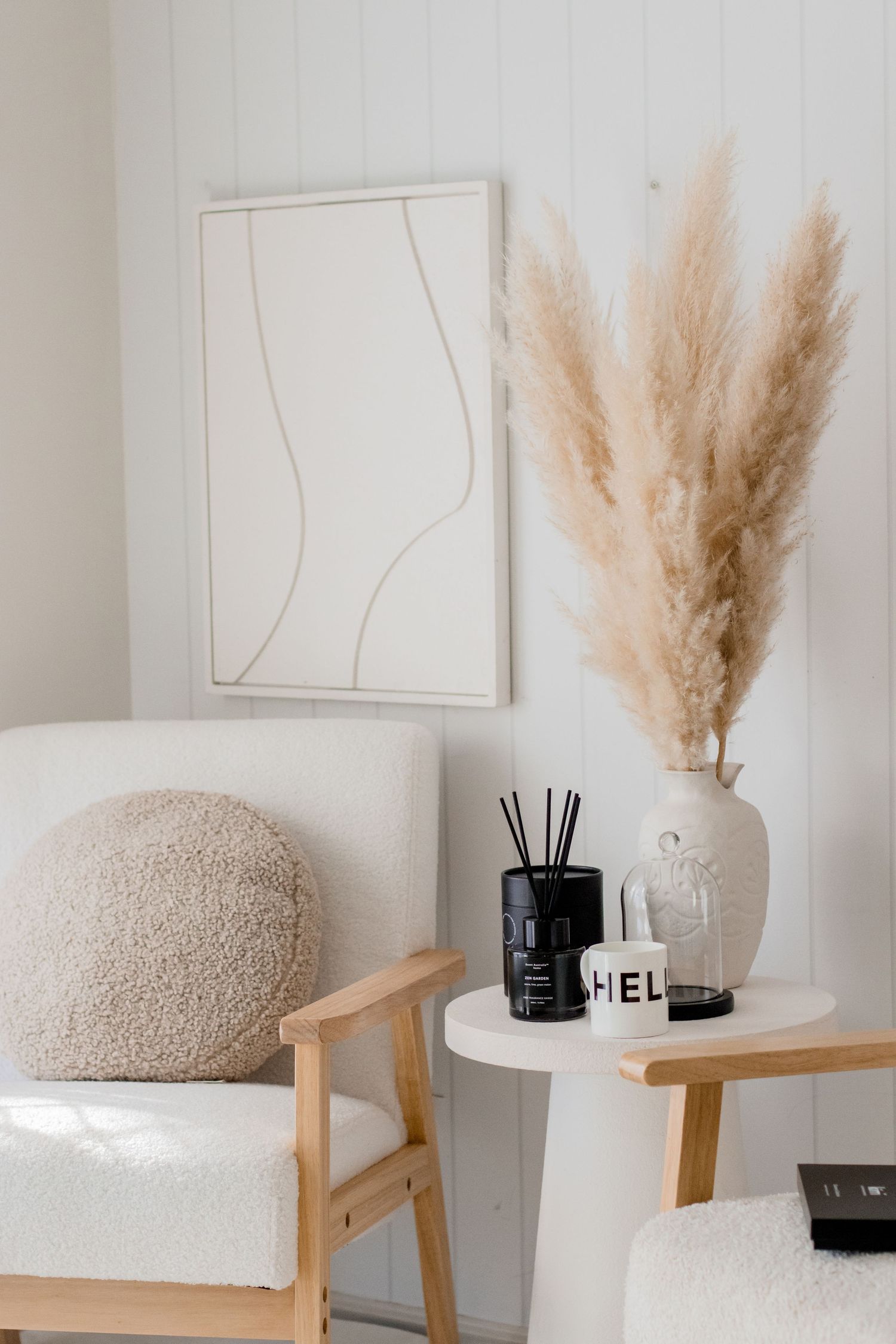 Modern chair with white sherpa cushion and pampas grass decor against minimal white wall with decorative accents.