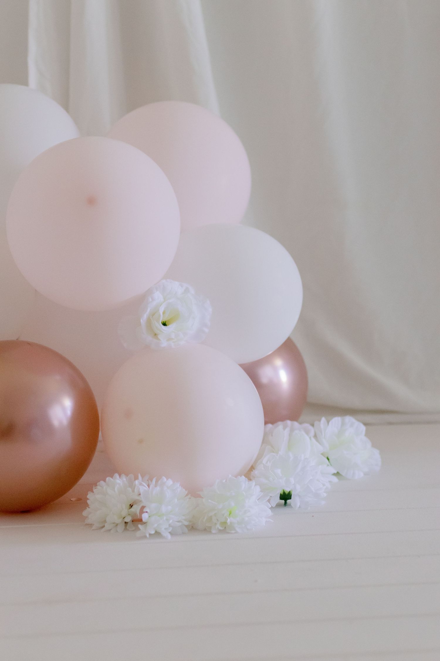 Pink and rose gold balloons arranged with white flowers against white backdrop.