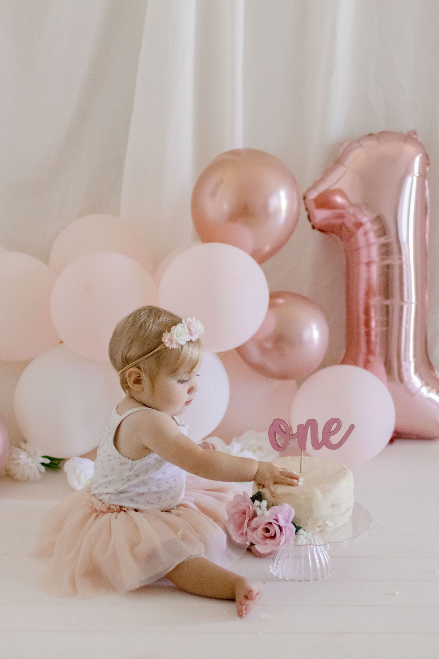 Delicate pink and white first birthday scene with balloon decorations and floral accents.