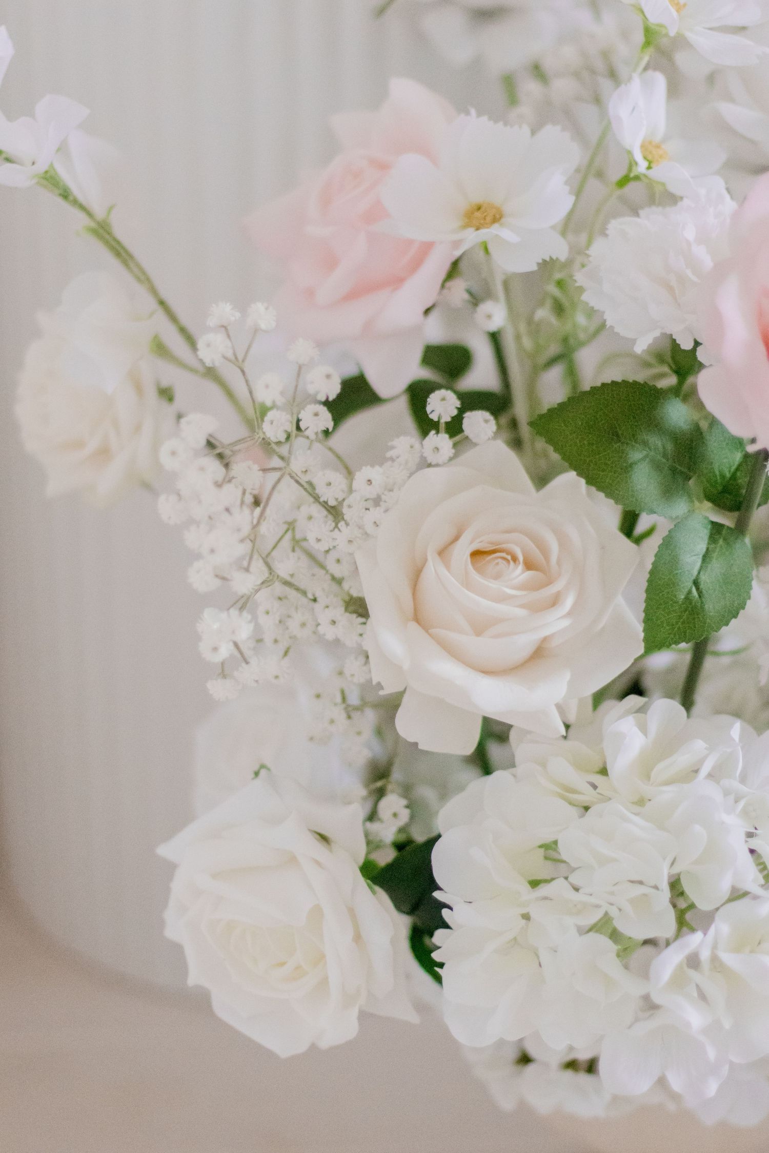 Delicate arrangement of white roses and baby's breath flowers in soft natural light.