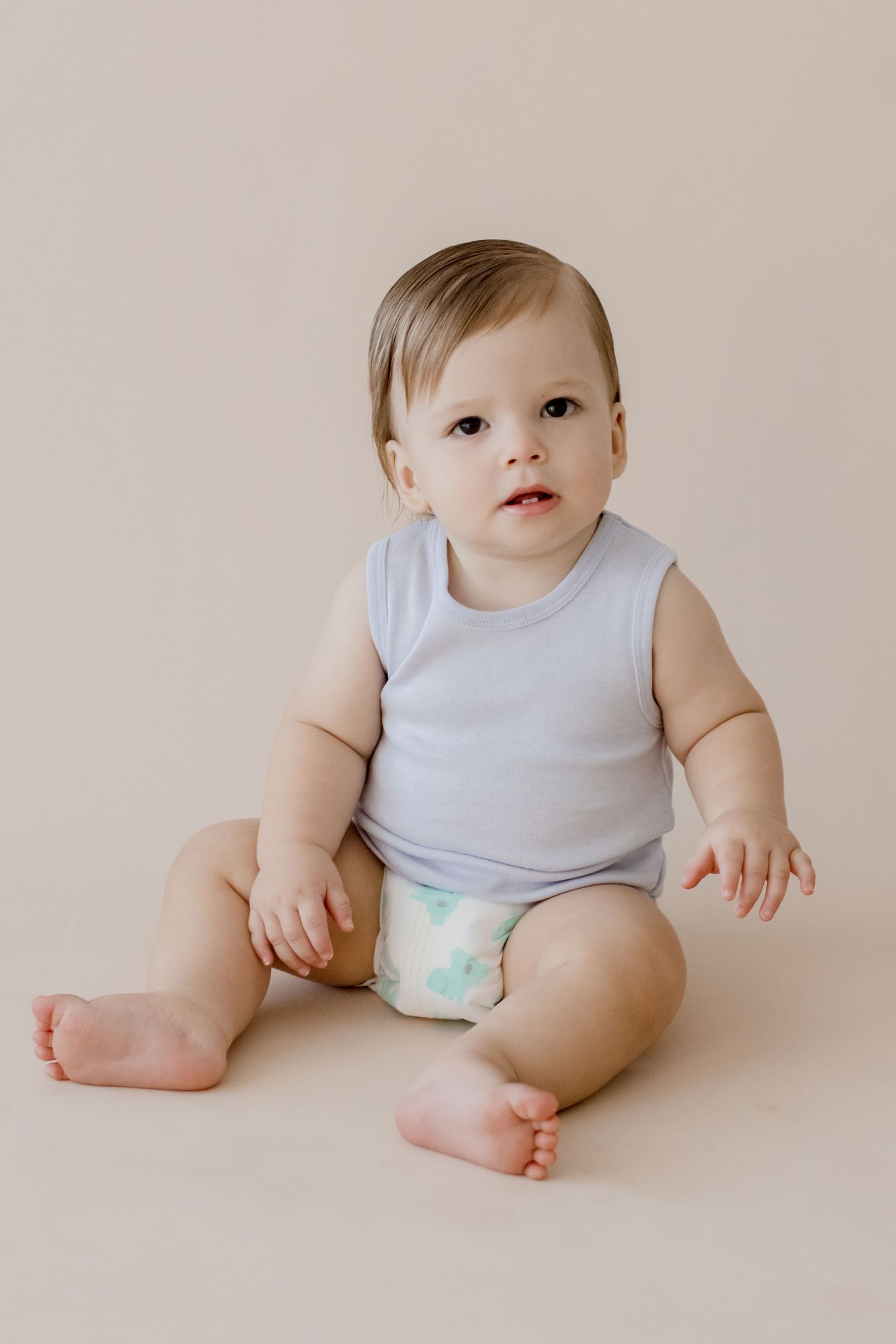 Baby in light blue sleeveless outfit sits on beige background.
