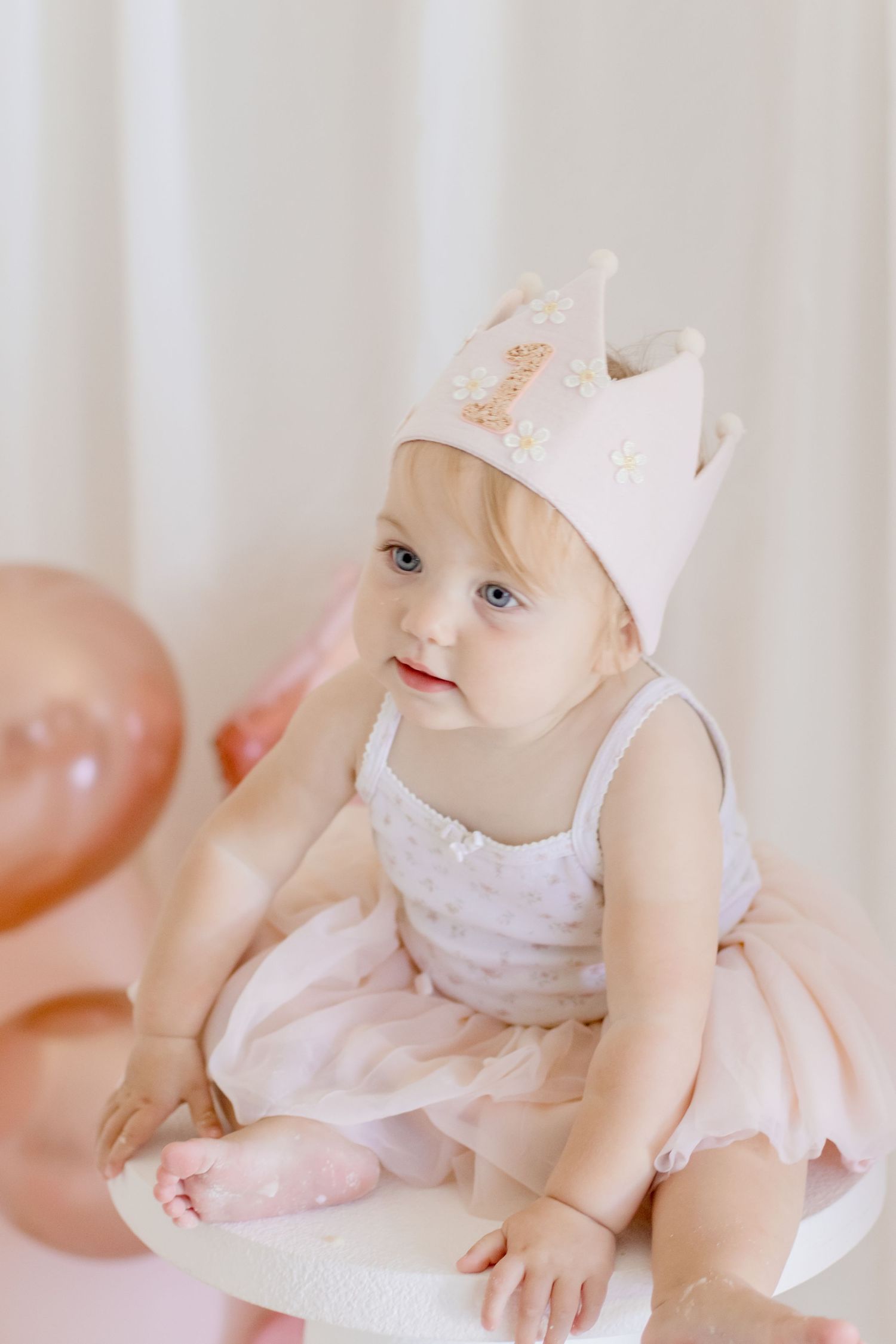 A delicate crown and tulle dress create a regal scene with peach balloons in the background.