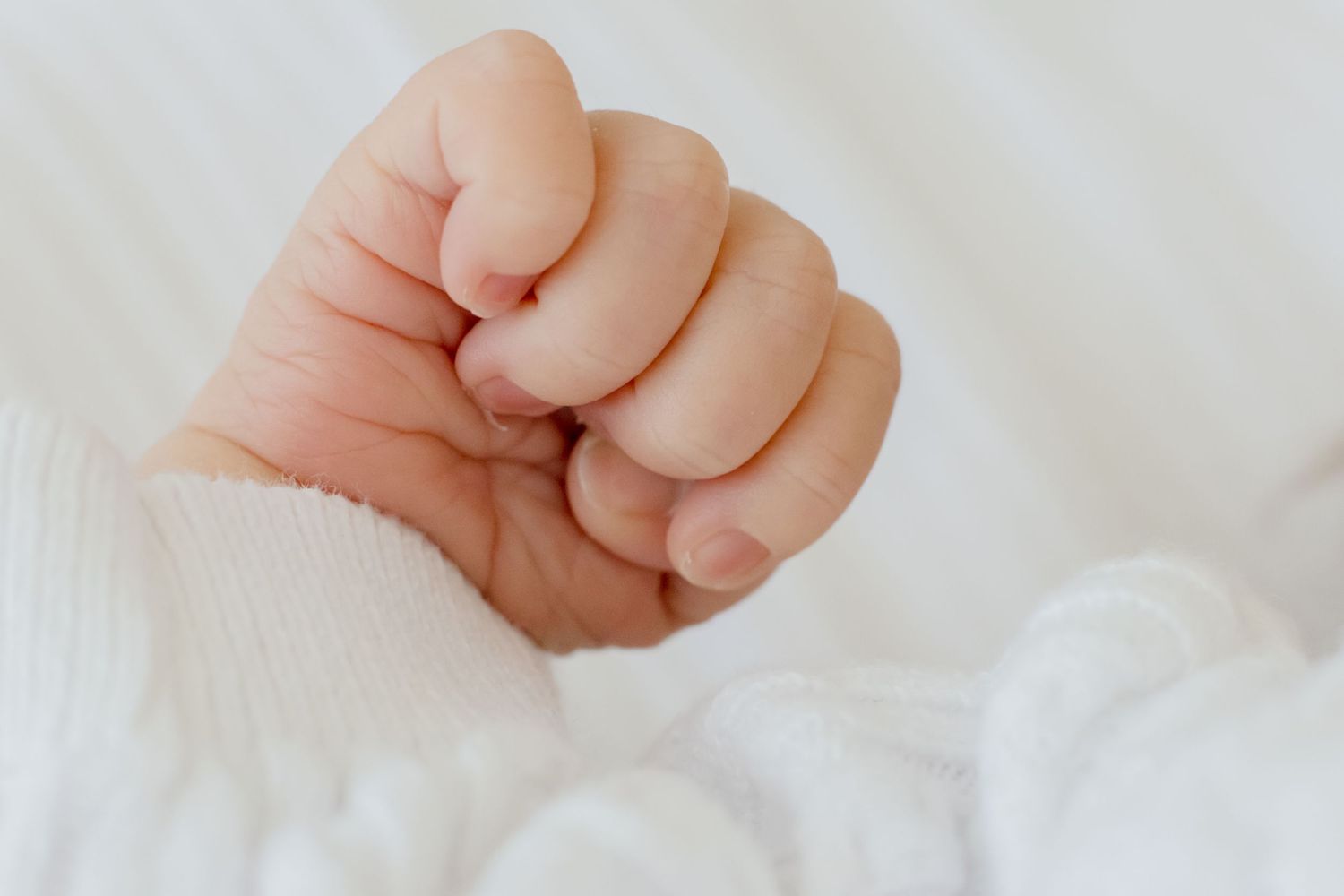 Close-up of tiny newborn baby's fist against white fabric.