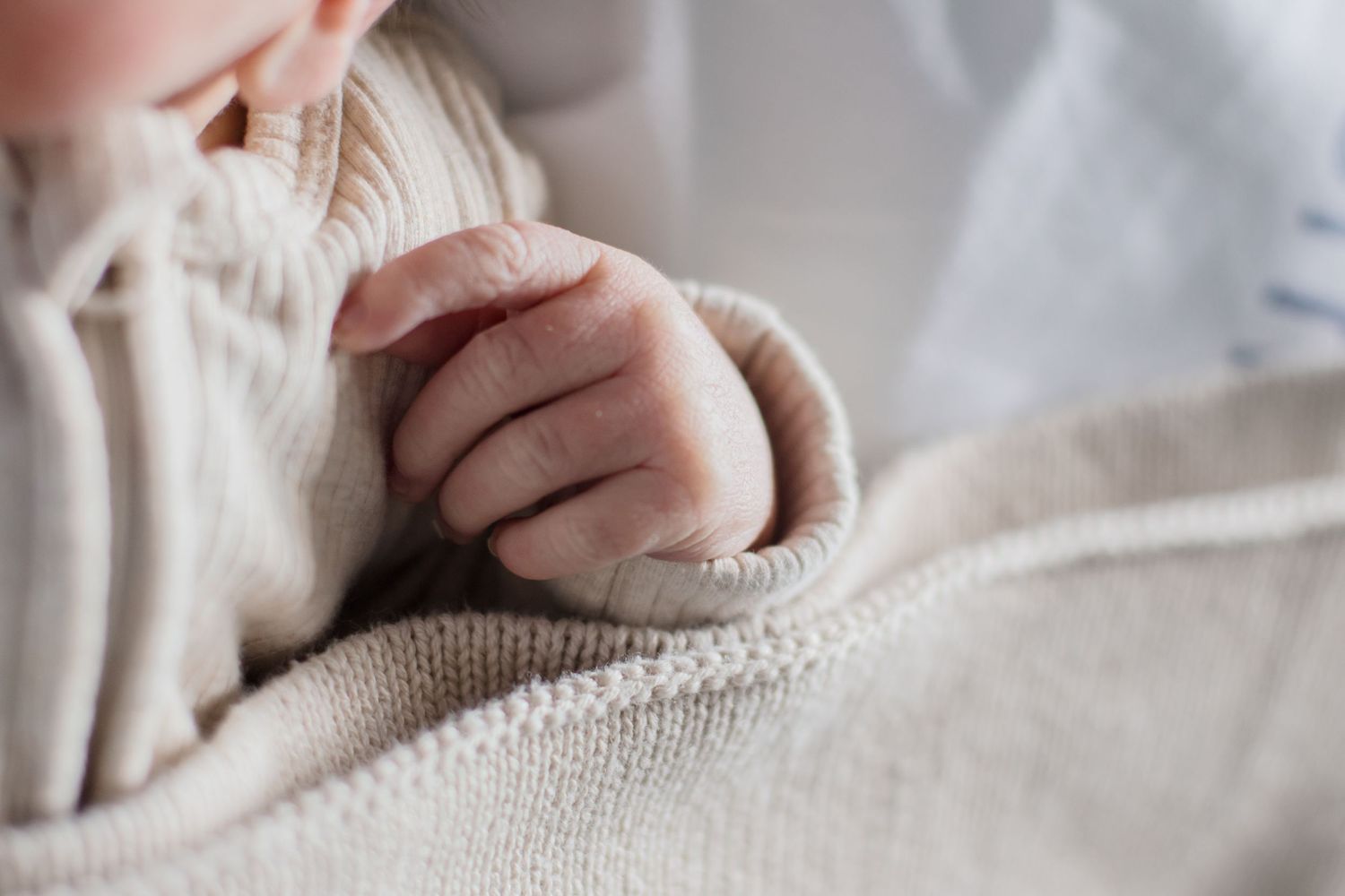 Close up of a tiny baby hand grasping against white knitted fabric.