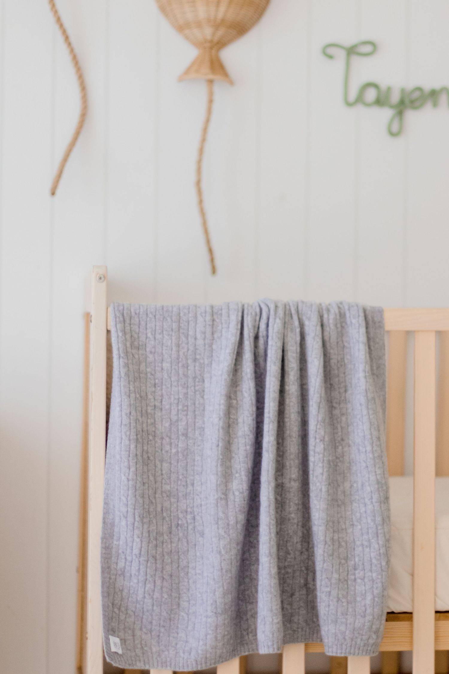 Tan balloon wall decorations and grey blanket draped over wooden crib rail.