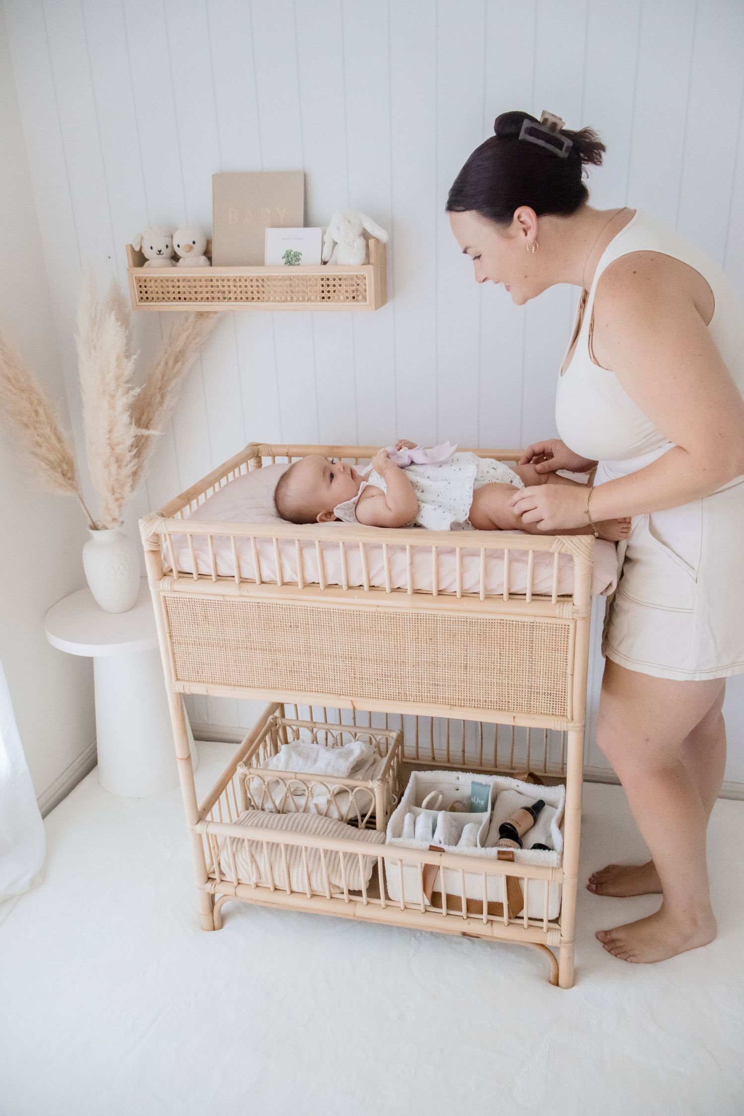 Nursery scene with rattan changing table and pampas grass decor in minimalist white room.