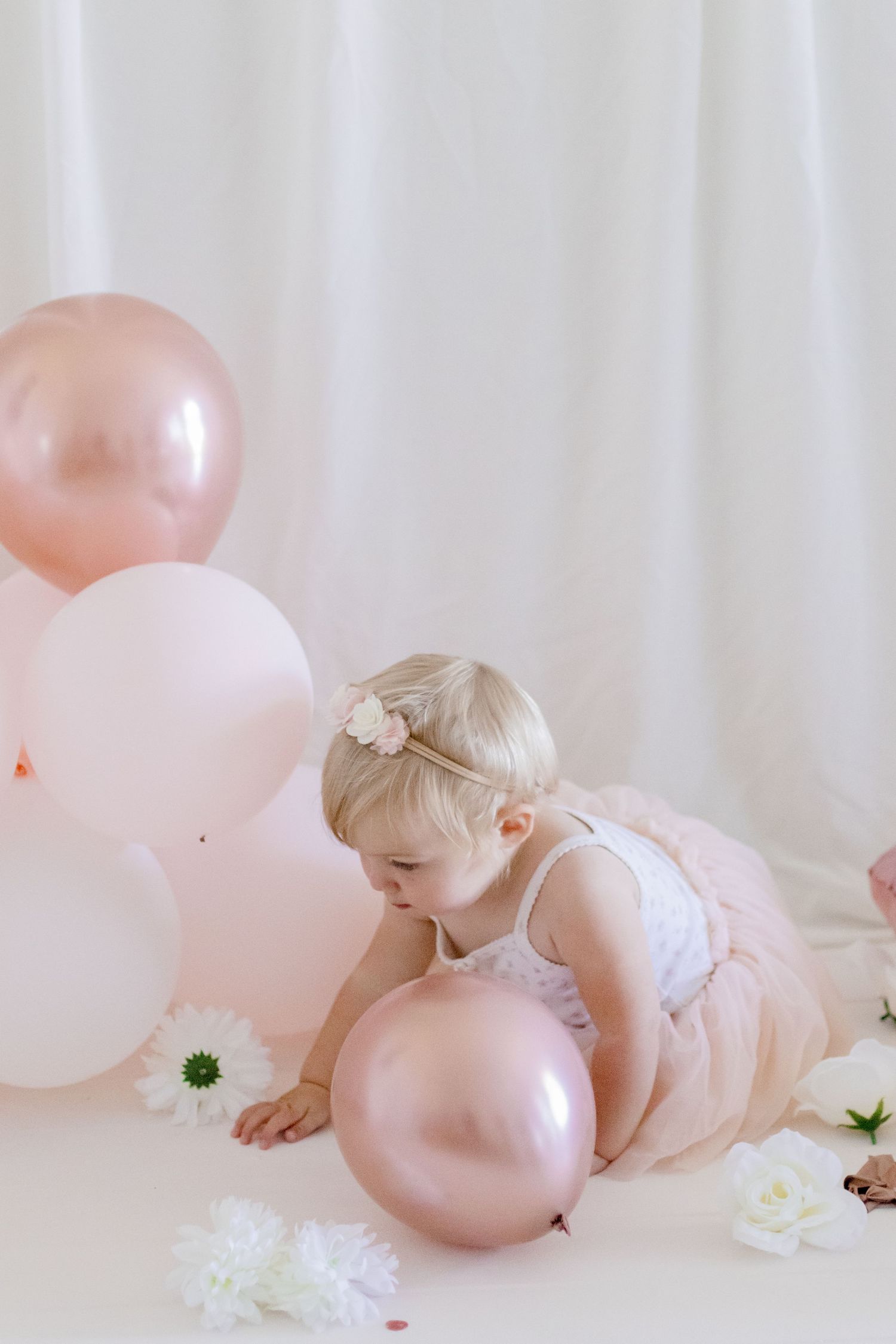 Little one in ballet outfit playing with pink balloons on white floor.