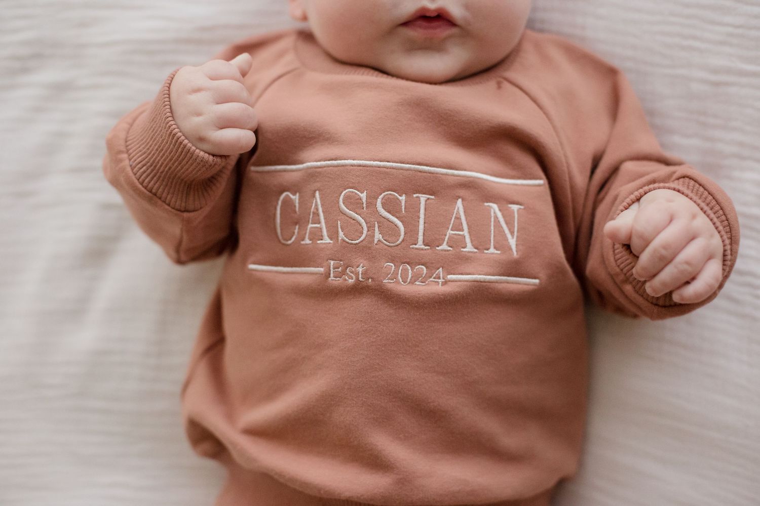 Baby wearing a dusty rose colored sweatshirt with name 'Cassian' printed across the front.