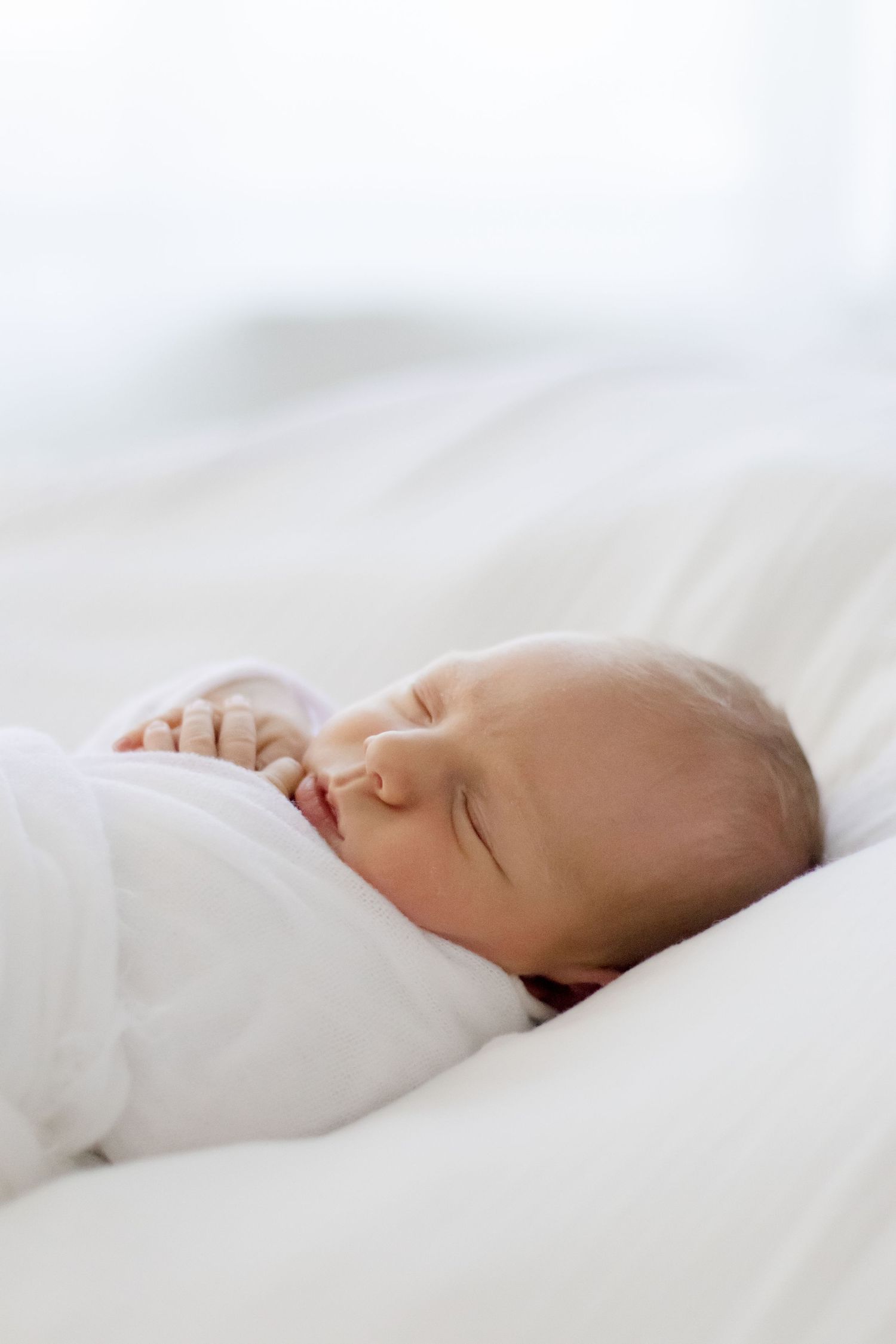 Peaceful newborn baby sleeping soundly on white bedding.