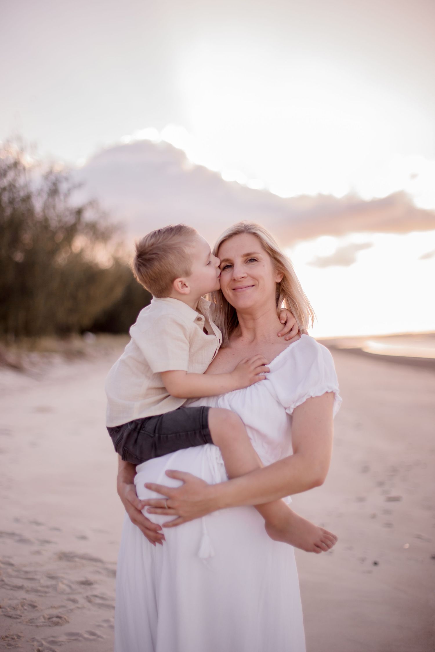 Joyful moment between mother and child sharing embrace on sandy beach at dusk.