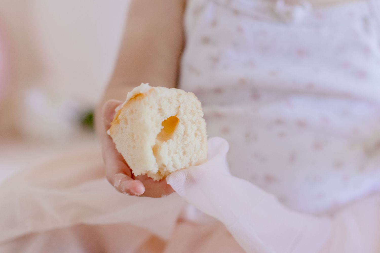 Close up of small hands holding piece of white bread against pink tulle dress.