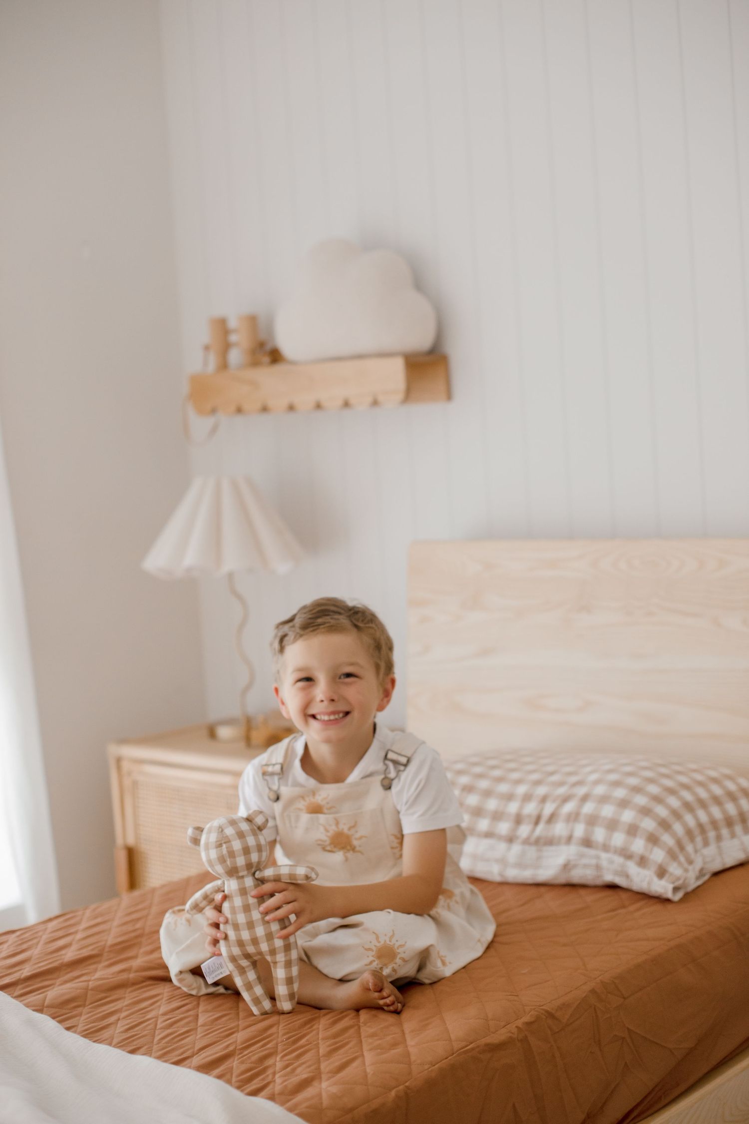 Cozy bedroom interior with plaid bedding, wooden shelf, and decorative lamp in neutral tones.