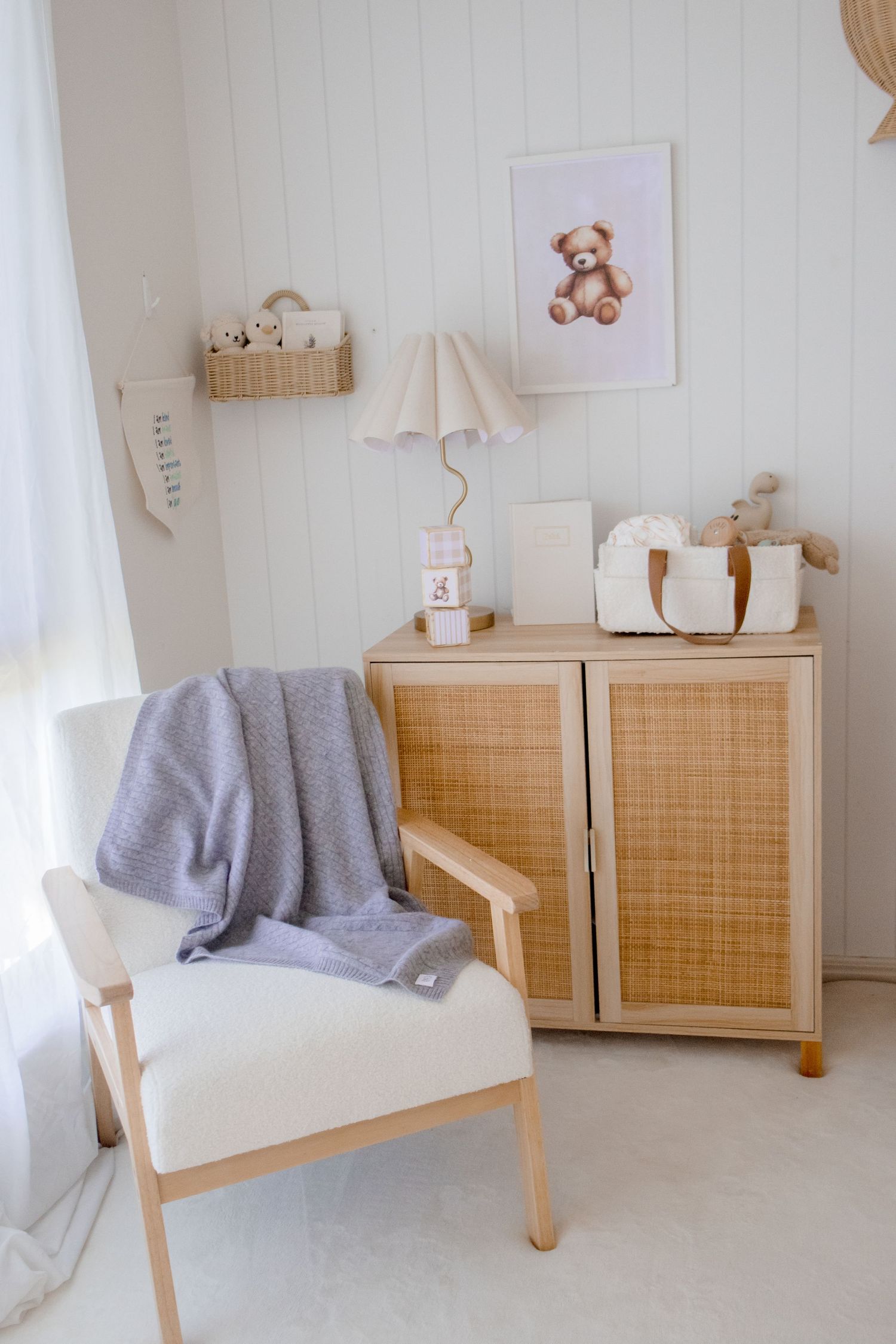 Scandinavian style nursery furniture with rattan details and gray throw blanket against white walls.