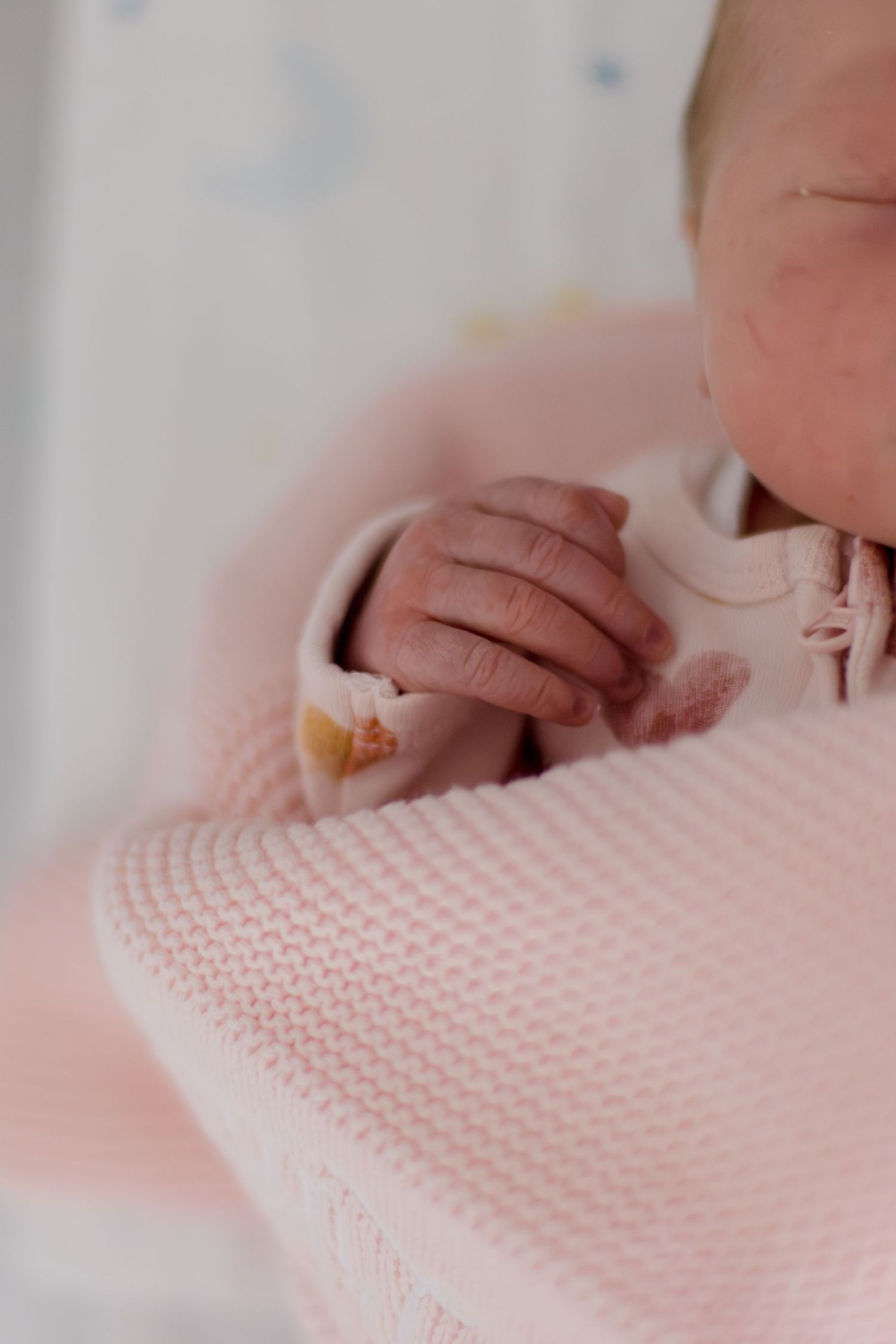 Close-up of a newborn baby's tiny hand wrapped in a soft pink knitted blanket.