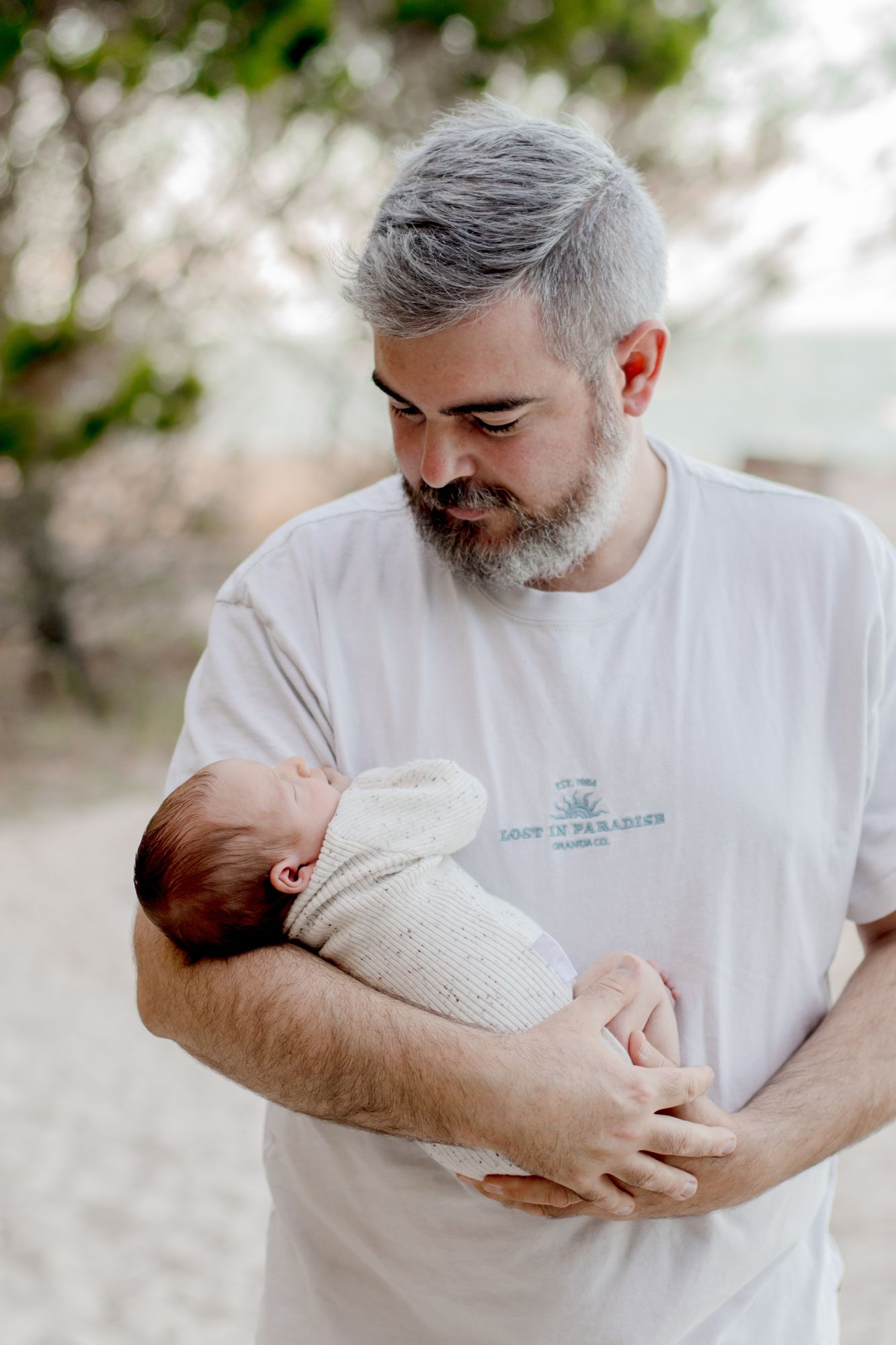 Person in white shirt tenderly holding and looking down at a swaddled newborn baby.