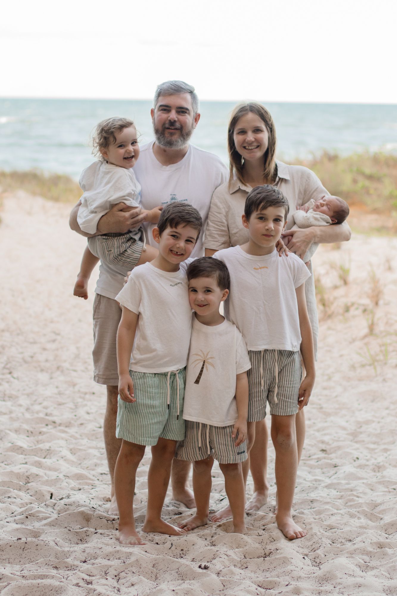 Family portrait on a beach with everyone wearing coordinating neutral colored clothing.