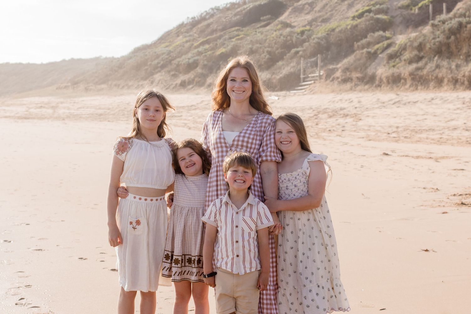 Group in coordinated vintage-style outfits posing for a portrait on a sandy beach with coastal cliffs behind them.