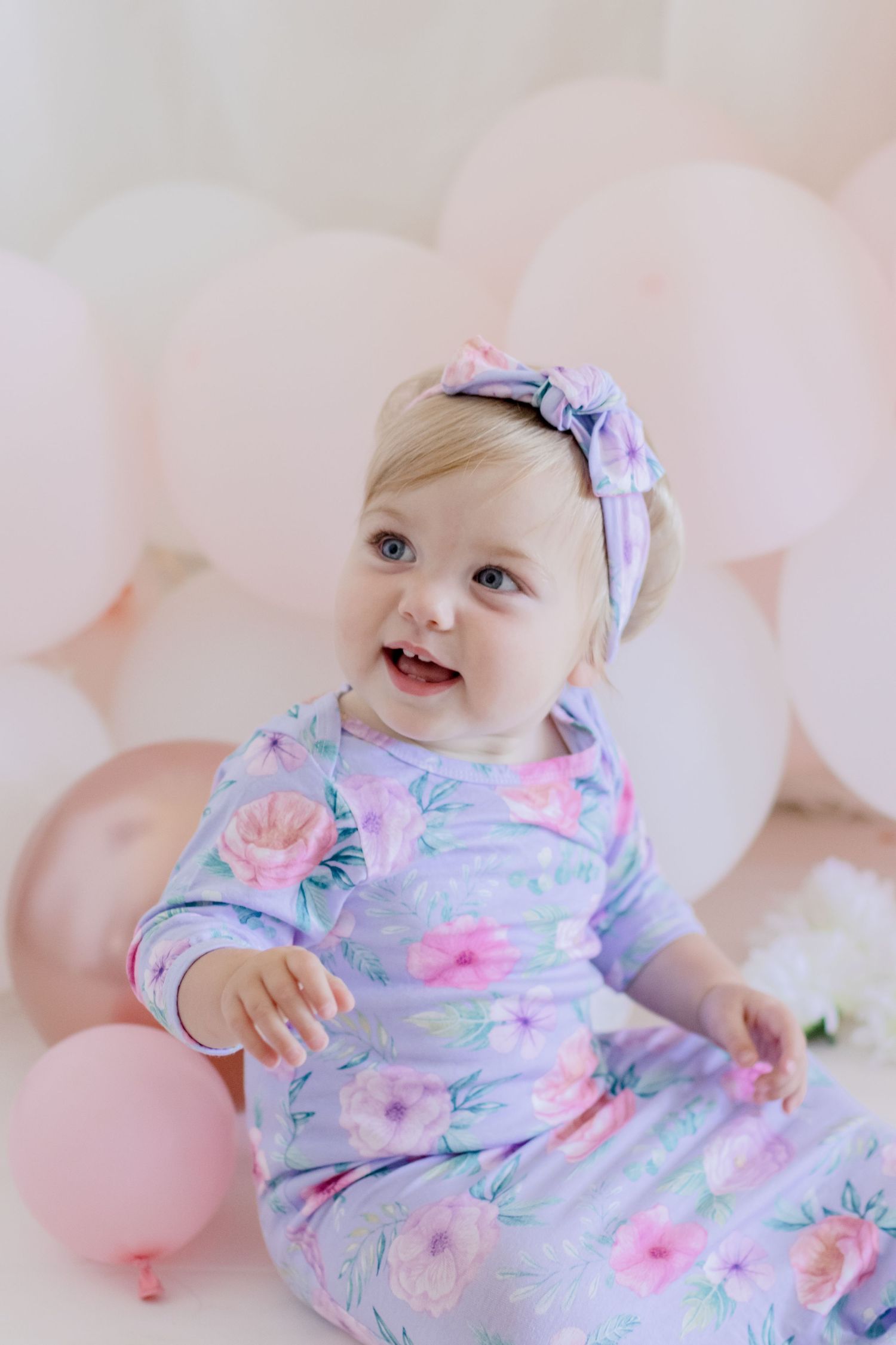 Baby in matching floral outfit and headband poses with pink balloons.