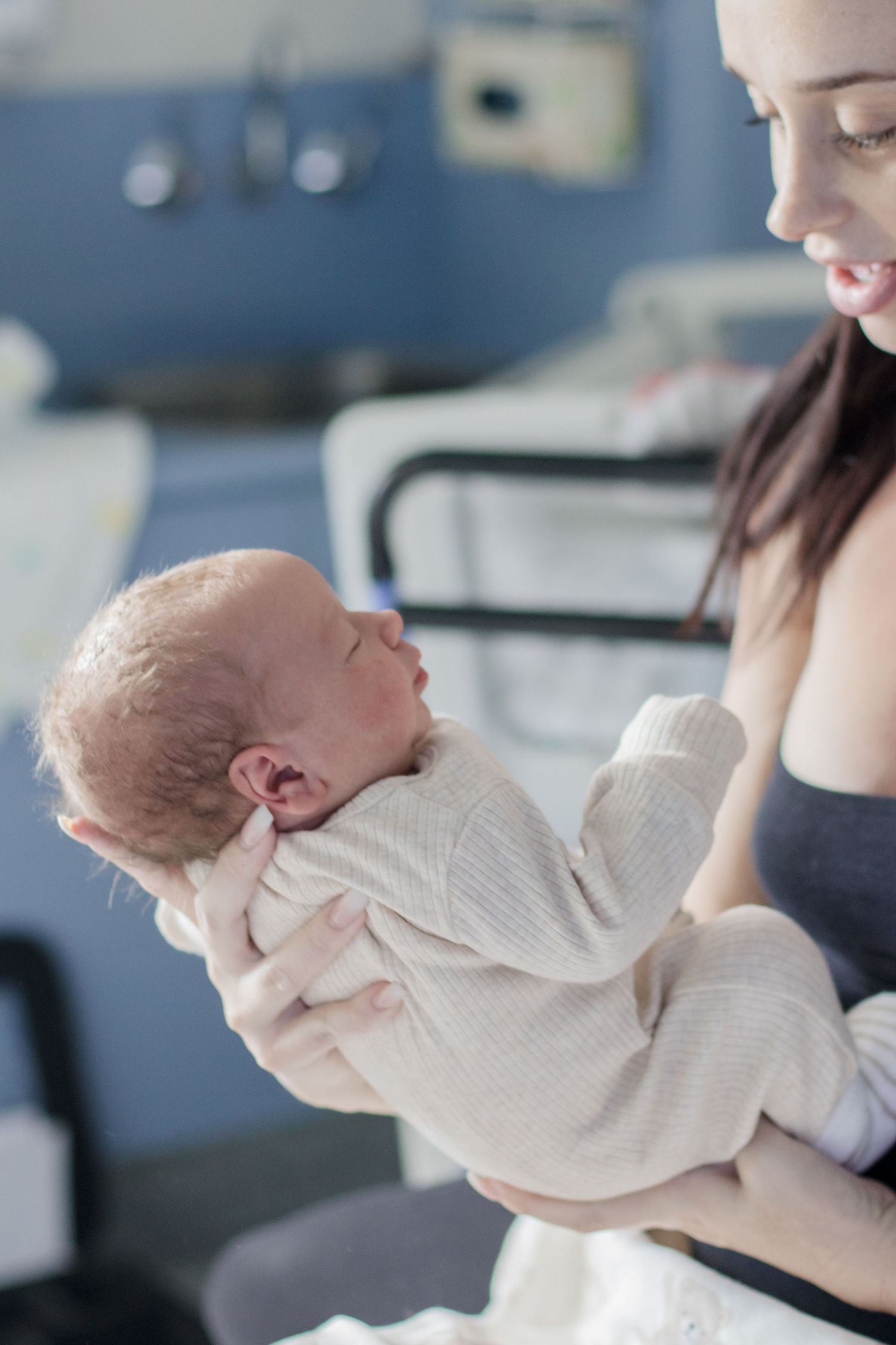 Newborn baby in cream sweater being cradled in hospital setting.