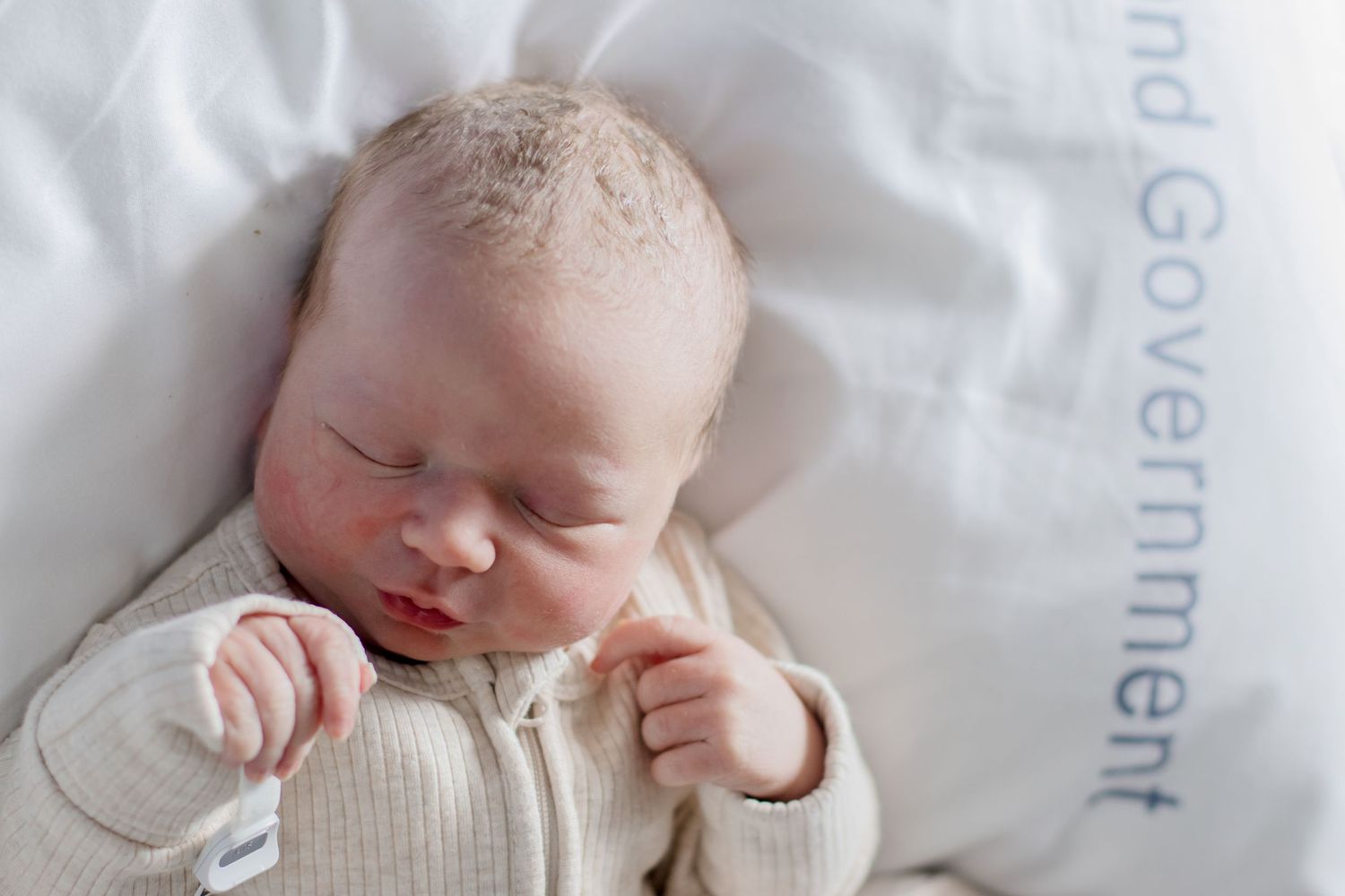 A sleeping infant wearing a cozy white knit outfit while resting on crisp white linens.