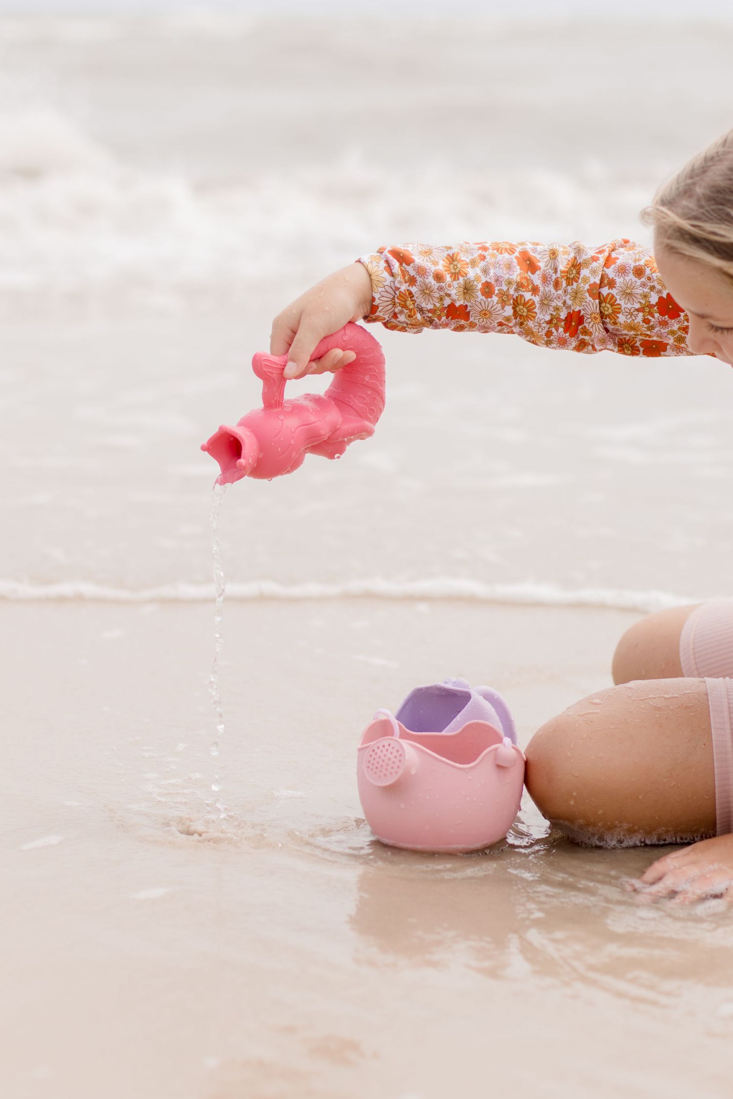 Close up of hands playing with pink sand toys in shallow beach water.