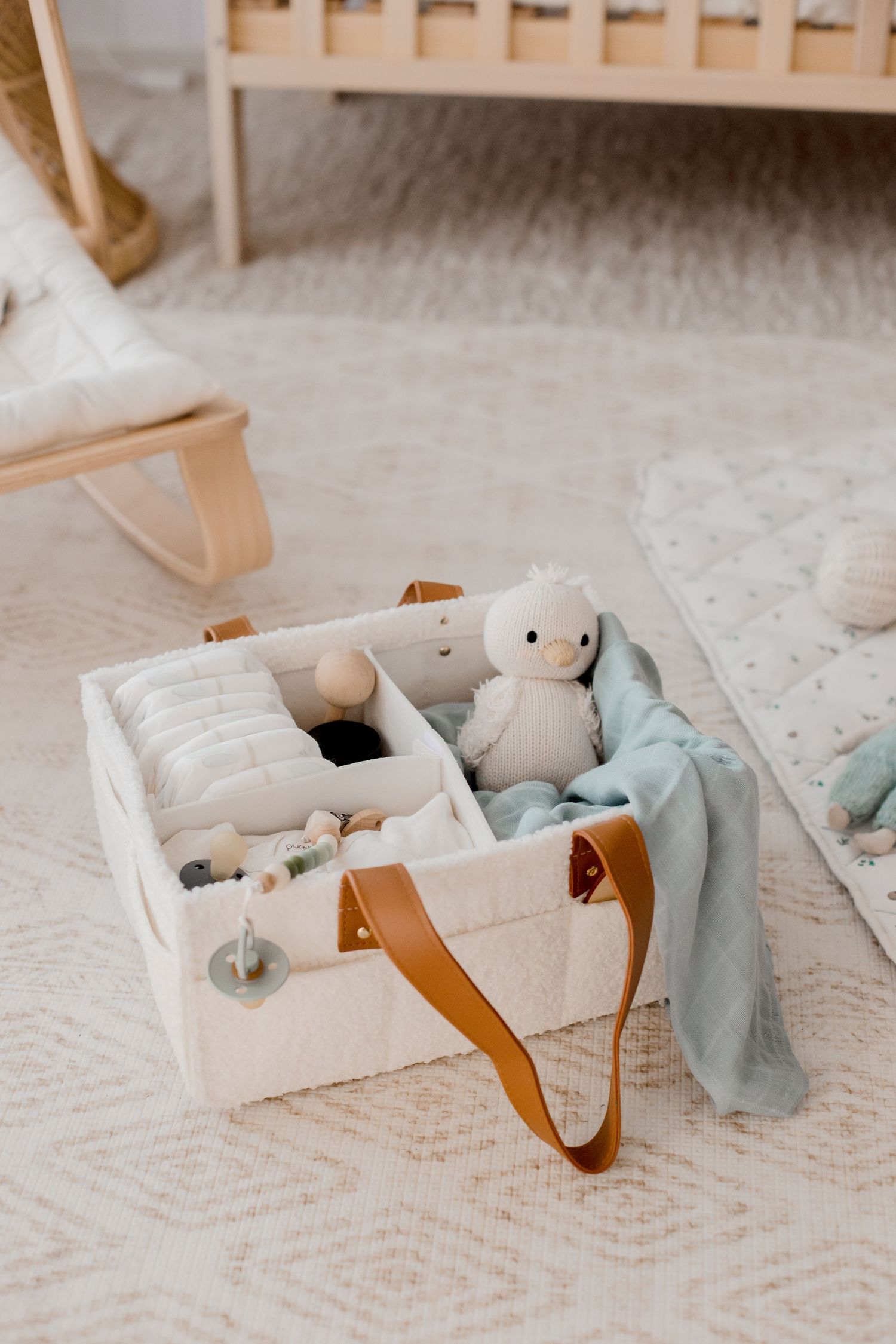 White storage basket with baby essentials, toys and blue blanket on patterned carpet.