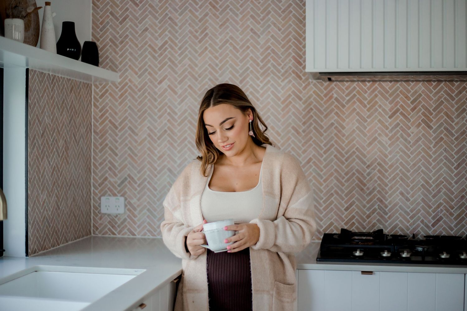 A person wearing a cozy cream sweater holds a white coffee mug while relaxing at home.