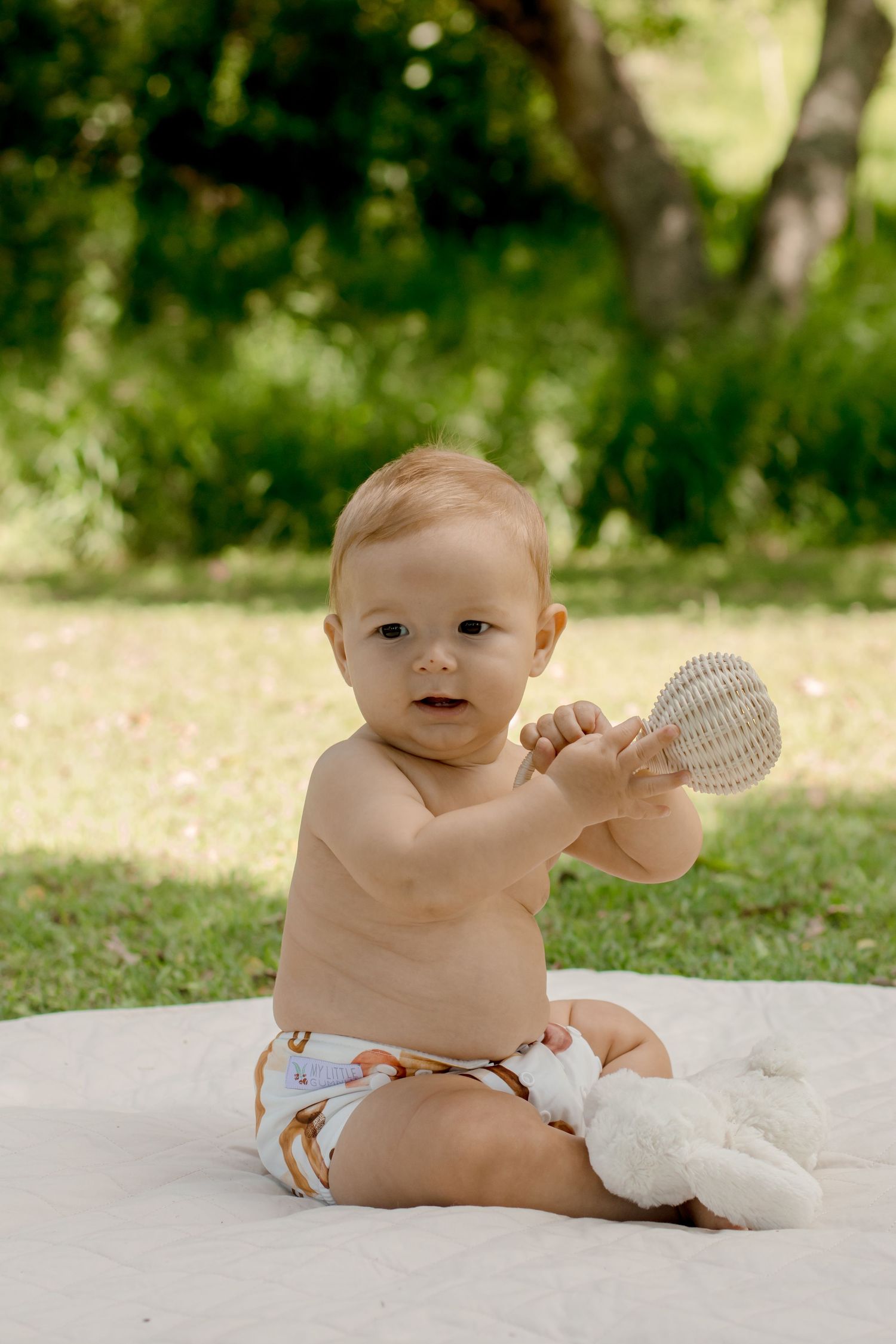Baby on white blanket outdoors holding a round object.