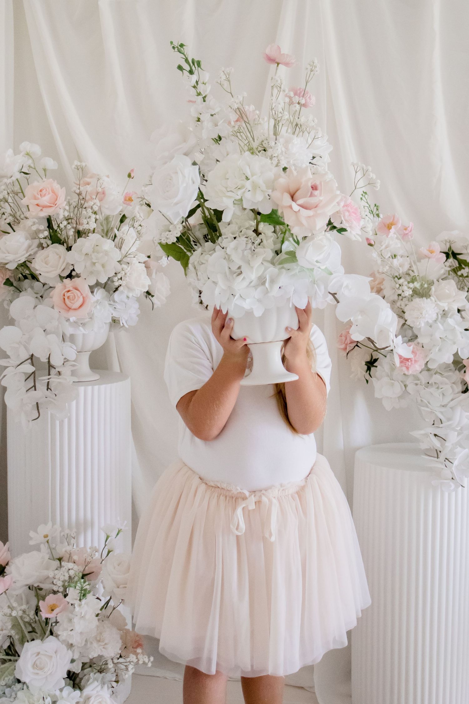 White and pink floral arrangement in classic urn style vase against white backdrop.