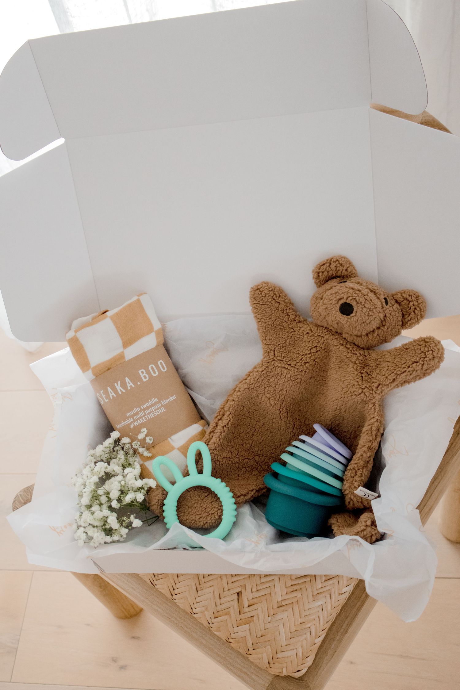 Open gift box containing teddy bear, teething ring, and baby essentials.