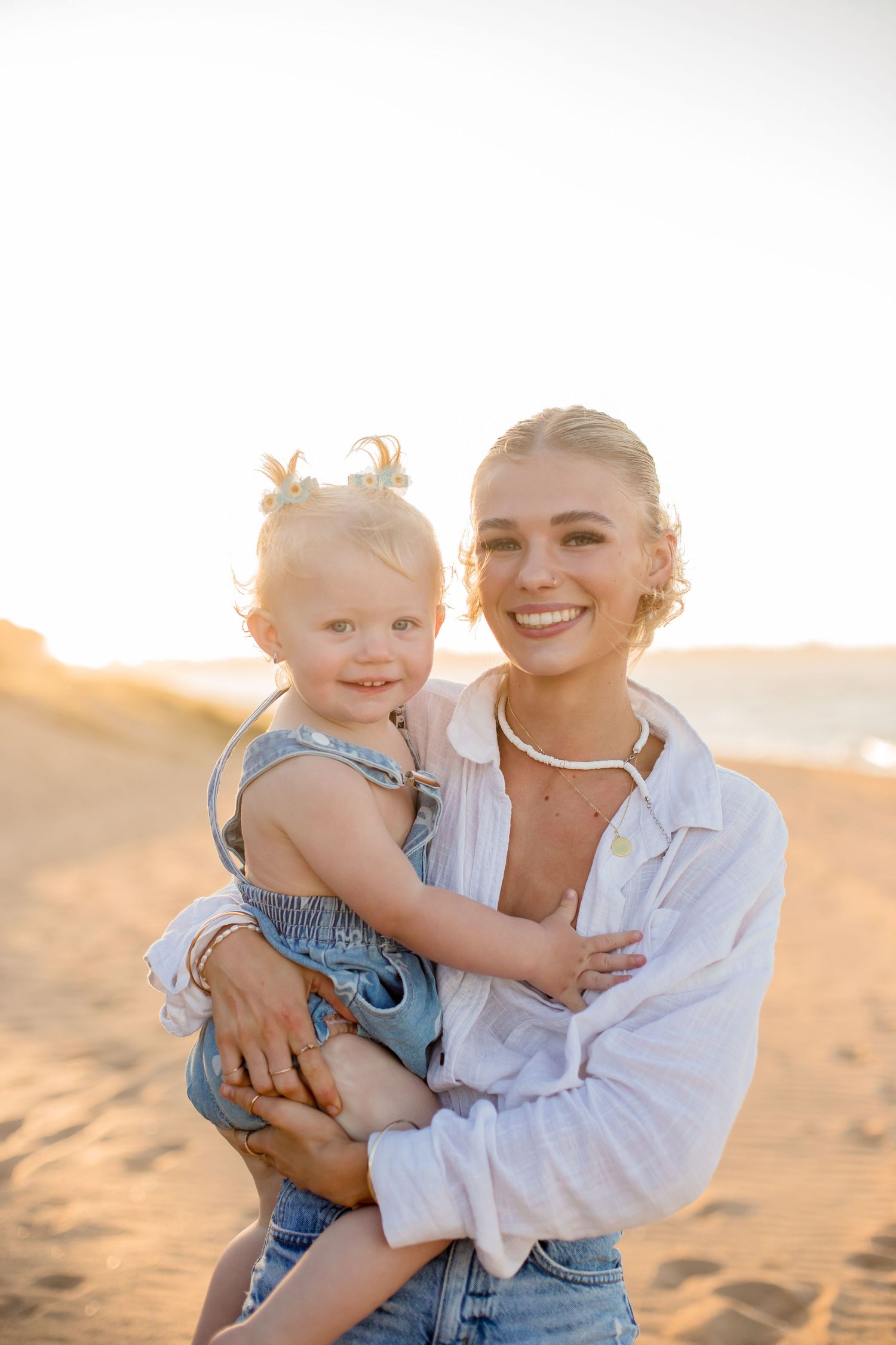 Mother and toddler in matching casual denim outfits sharing happy moment on beach.