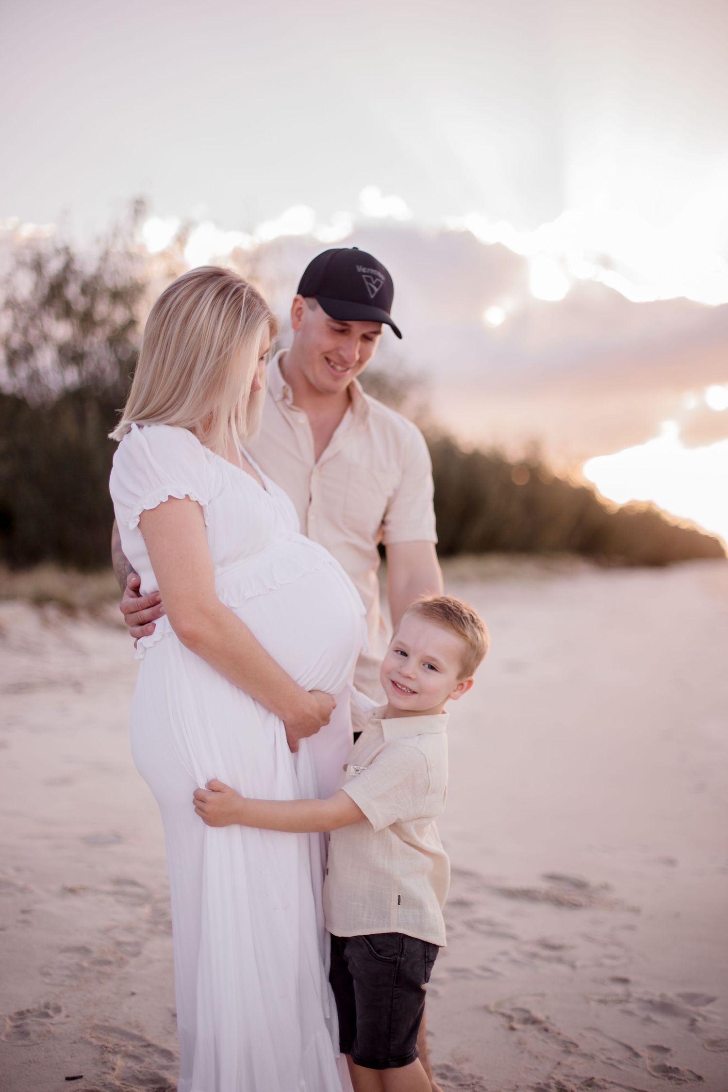 An intimate beachside maternity portrait with a child embracing mother's pregnant belly.