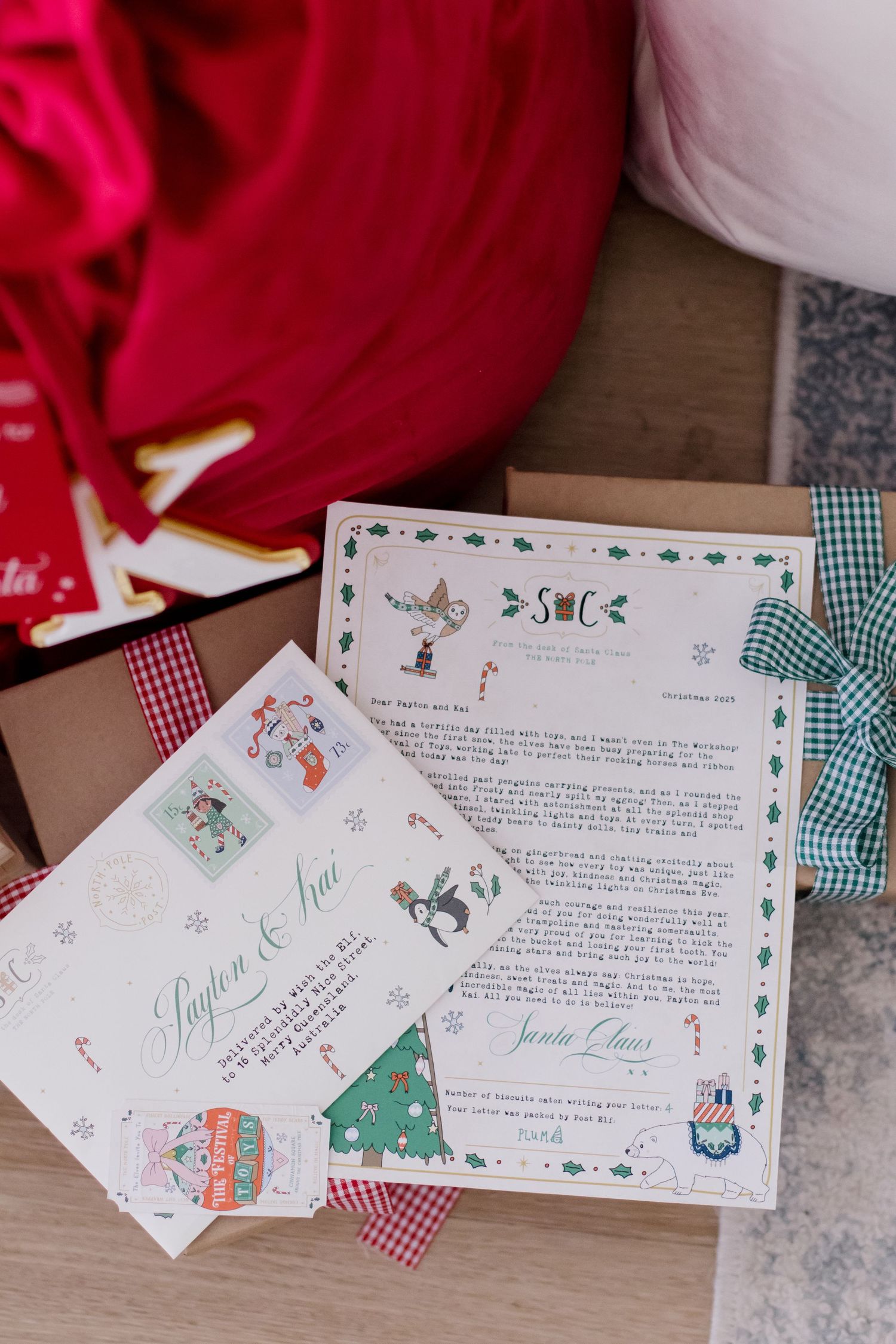 Holiday-themed letters and cards with cute illustrations spread out on wooden surface next to red fabric.