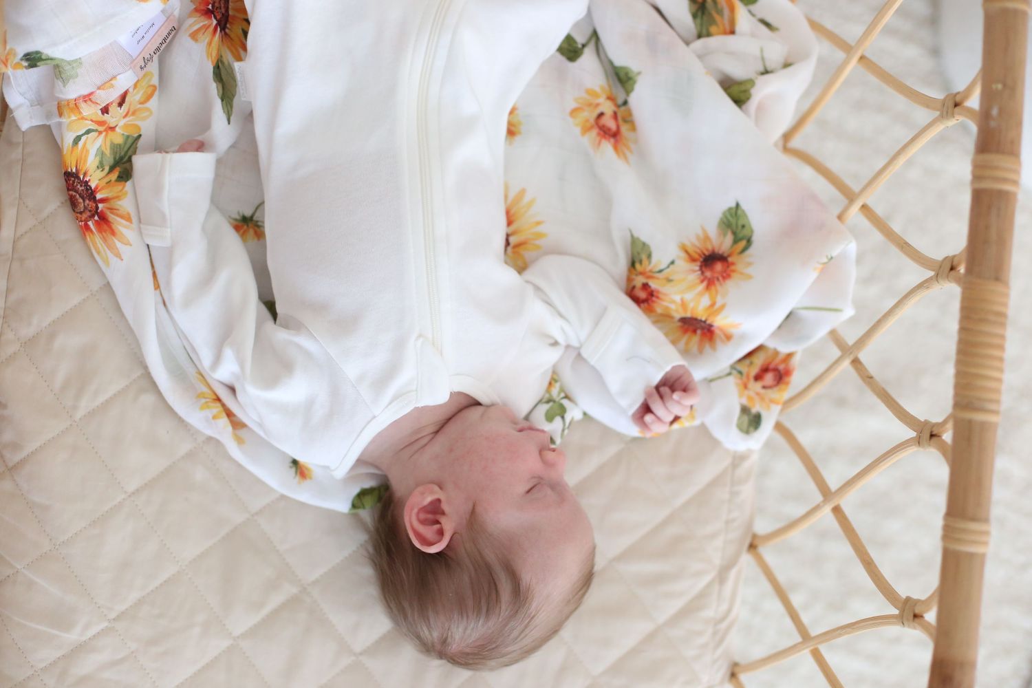 Overhead view of infant lying on white and floral patterned blanket.