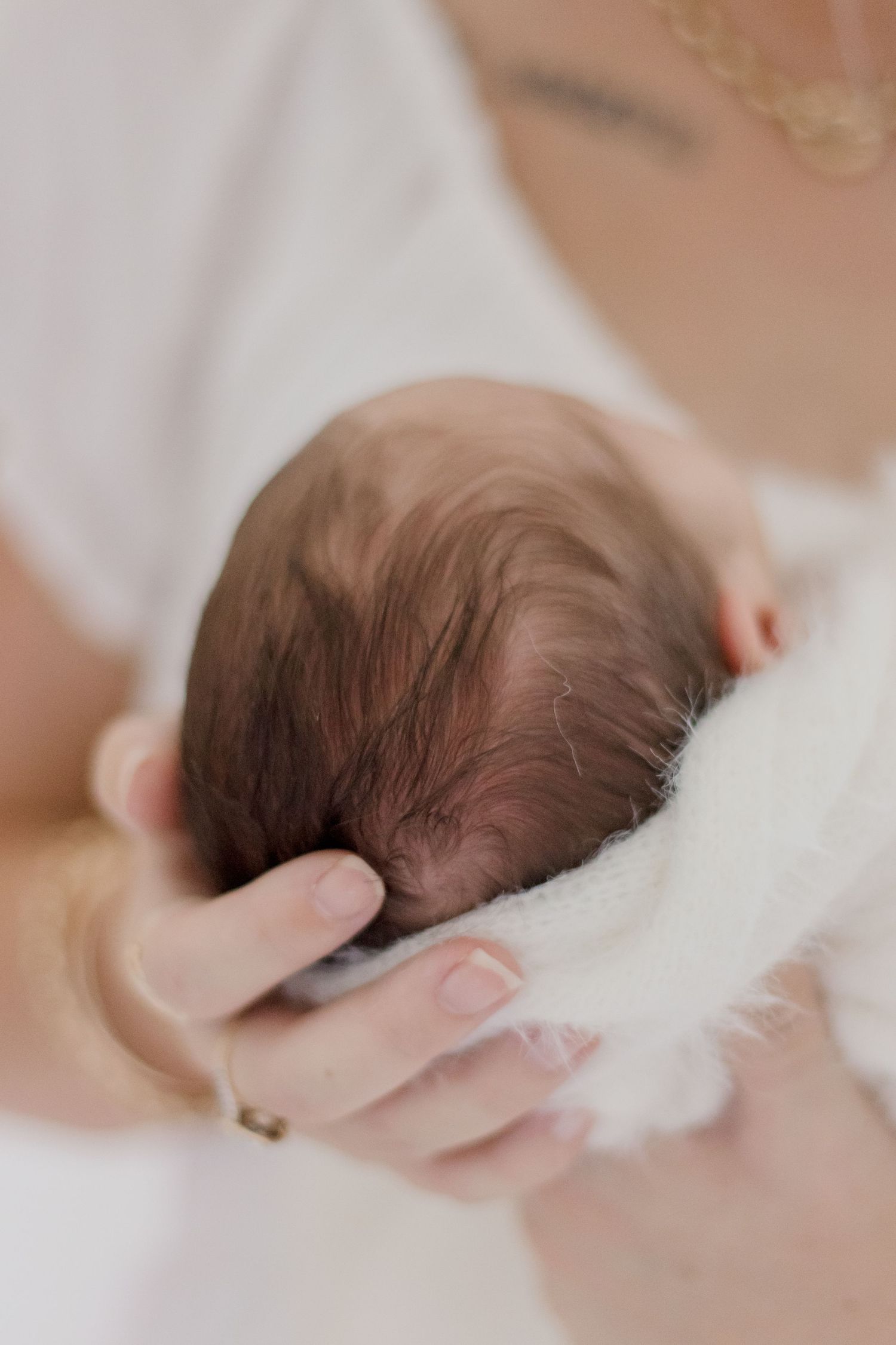 Gentle hand cradling newborn baby's head wrapped in white blanket.
