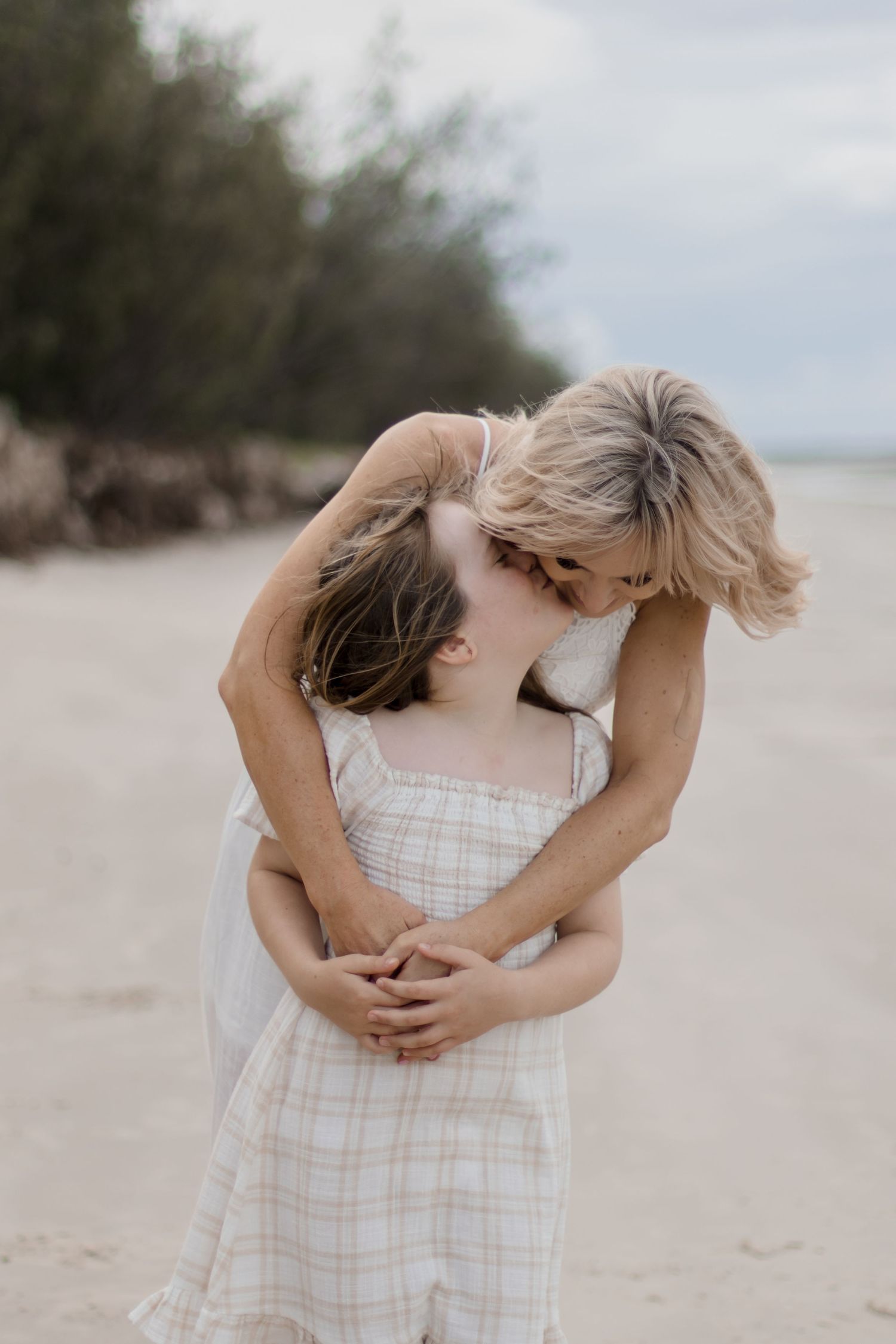 A tender embrace between two people in light summer clothing on a sandy beach.
