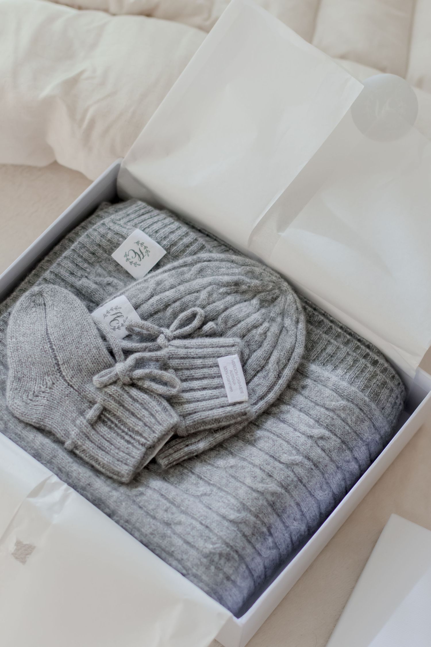 Neatly folded grey knit baby clothing and accessories arranged in white packaging.