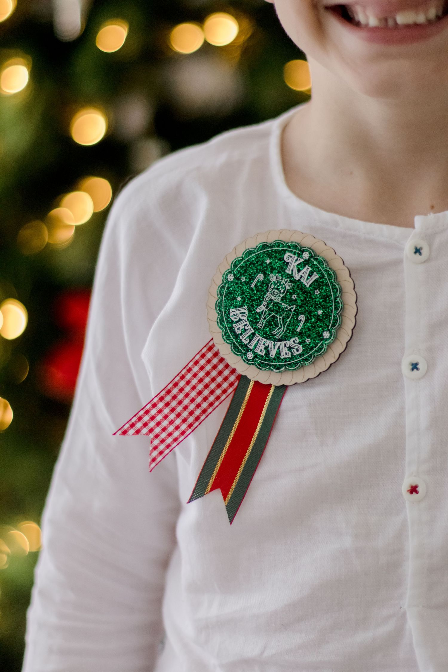 Decorative Christmas pins with red and white gingham ribbons displayed on white shirts against a bokeh background.