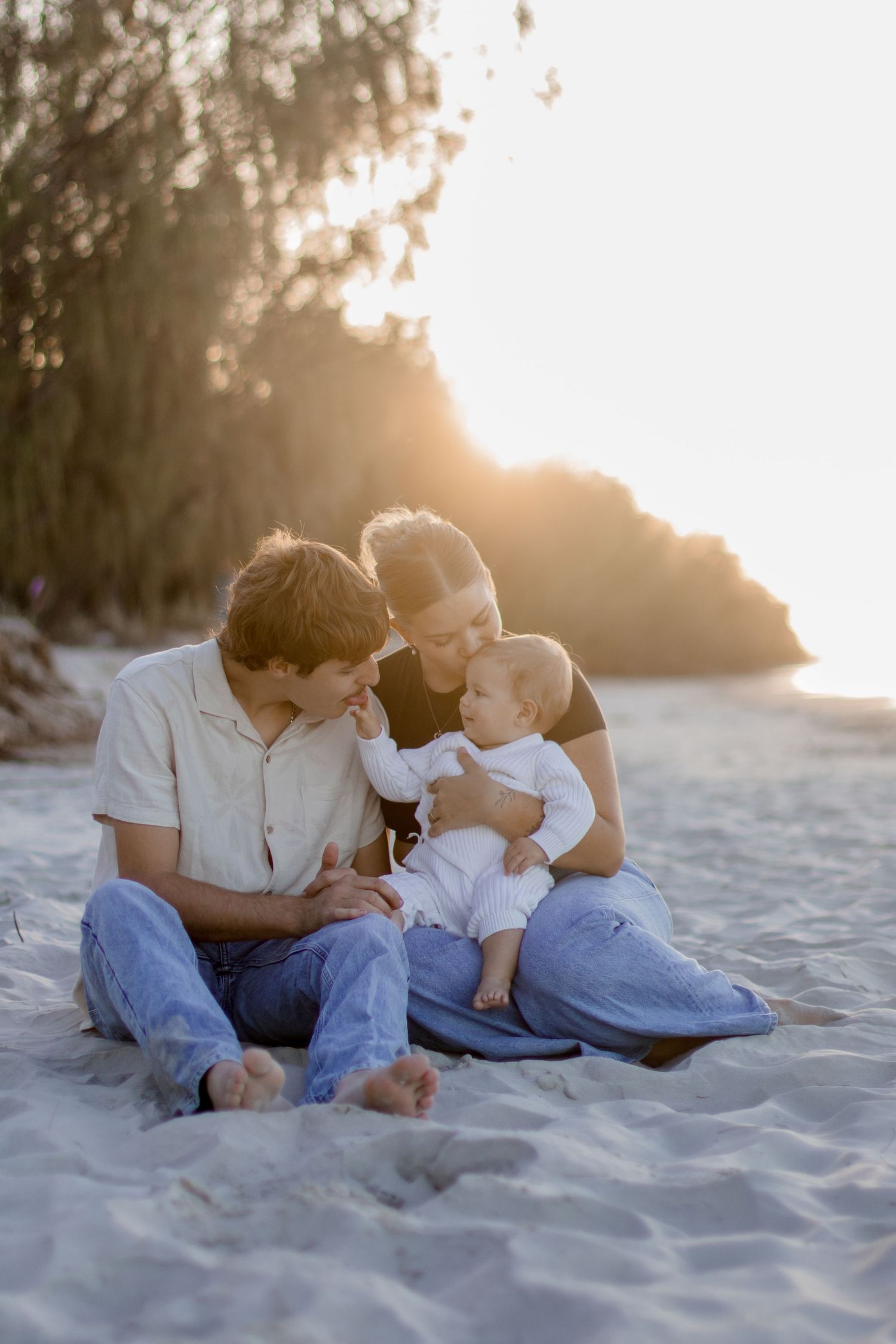 A loving family sits together on a sandy beach at sunset creating an intimate moment in warm golden light.