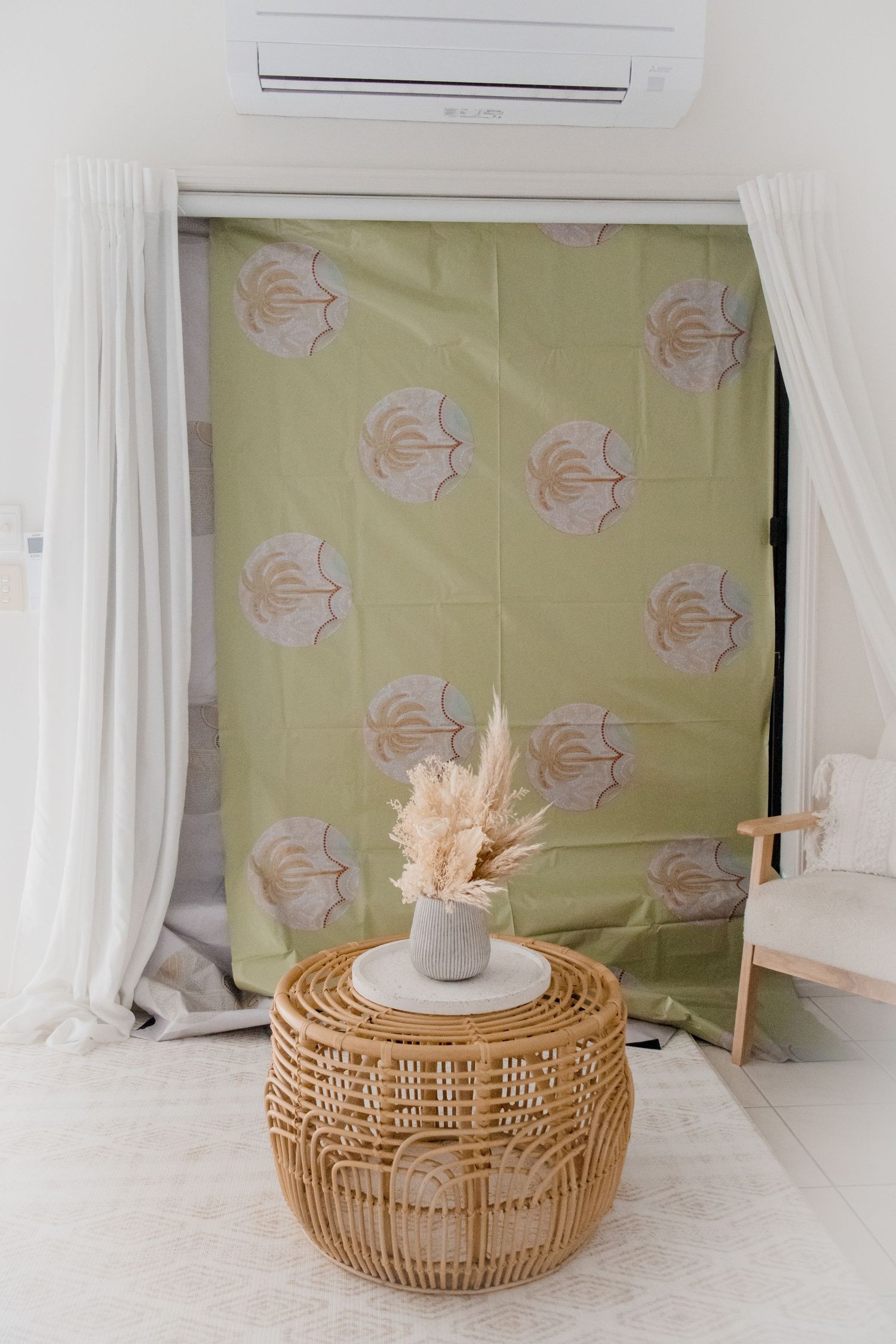 Modern interior with rattan table, dried flowers, and floral print backdrop near an air conditioner.