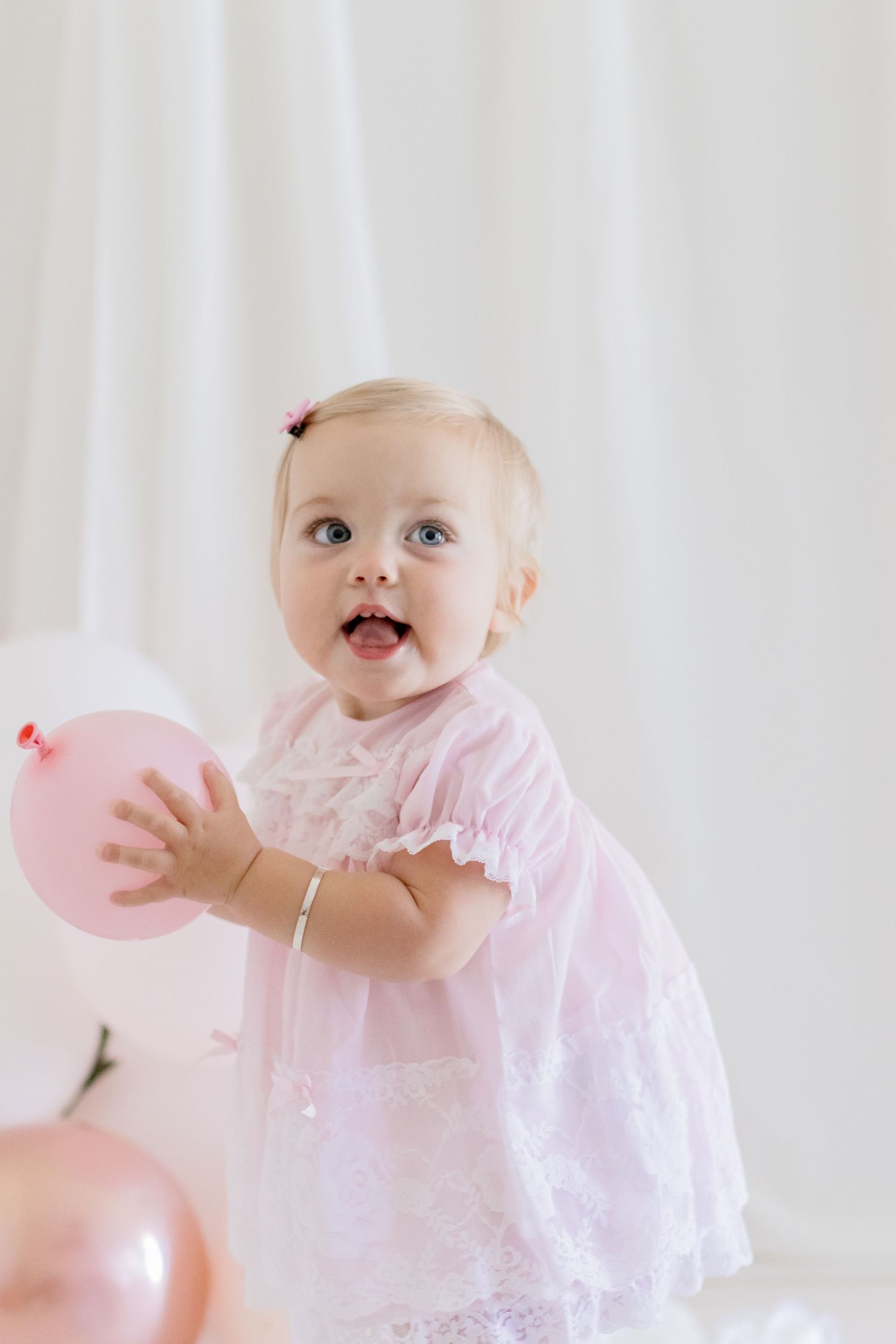 Joyful toddler in pink dress plays with balloon during portrait session.