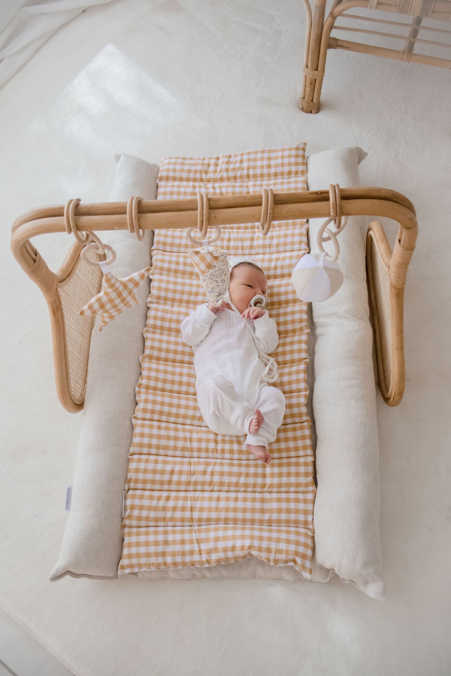 Overhead view of a baby lying on a gingham patterned changing pad with curved wooden rods and white accessories.