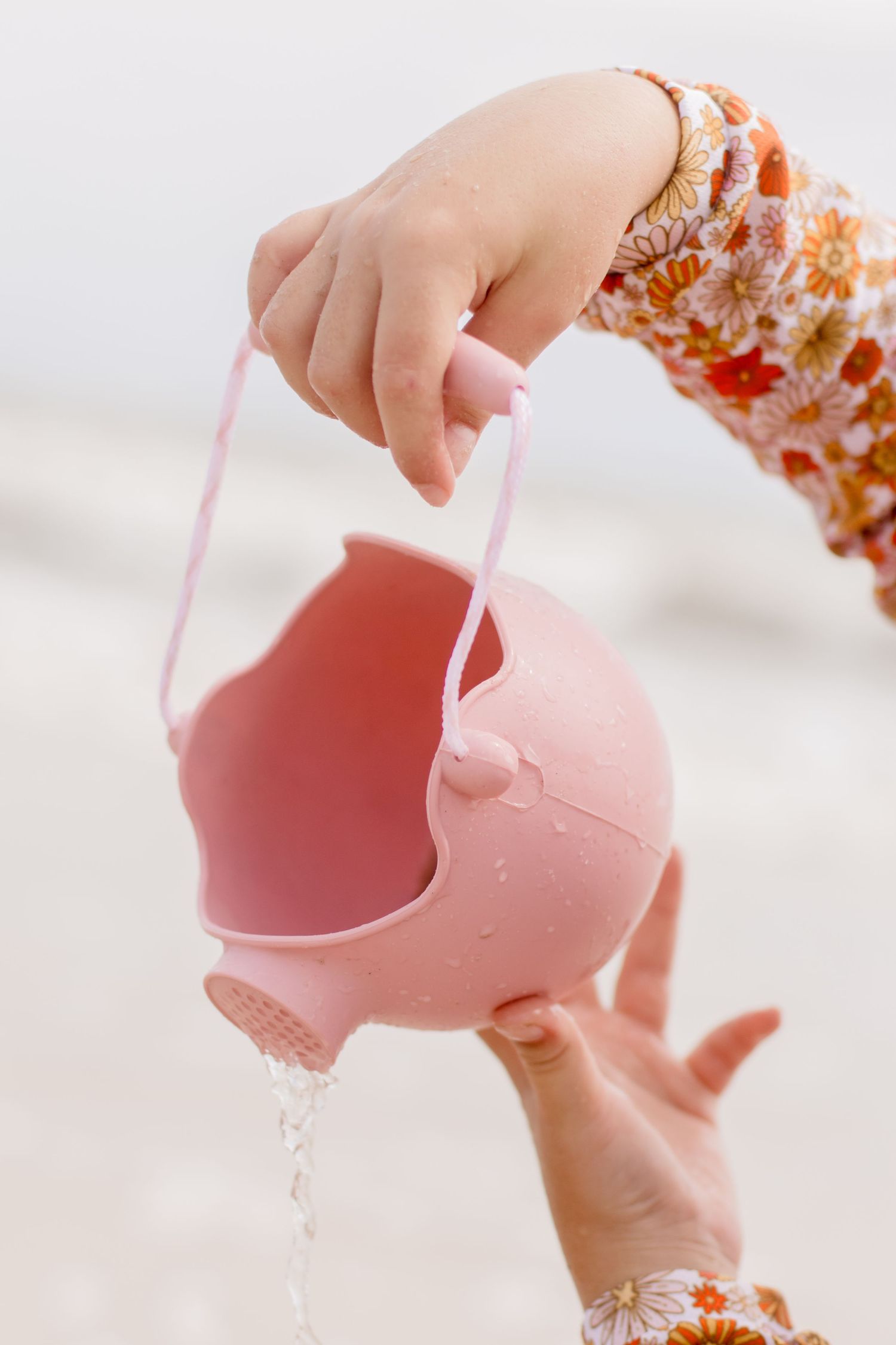 Pink whale-shaped watering toy being held against bright background.