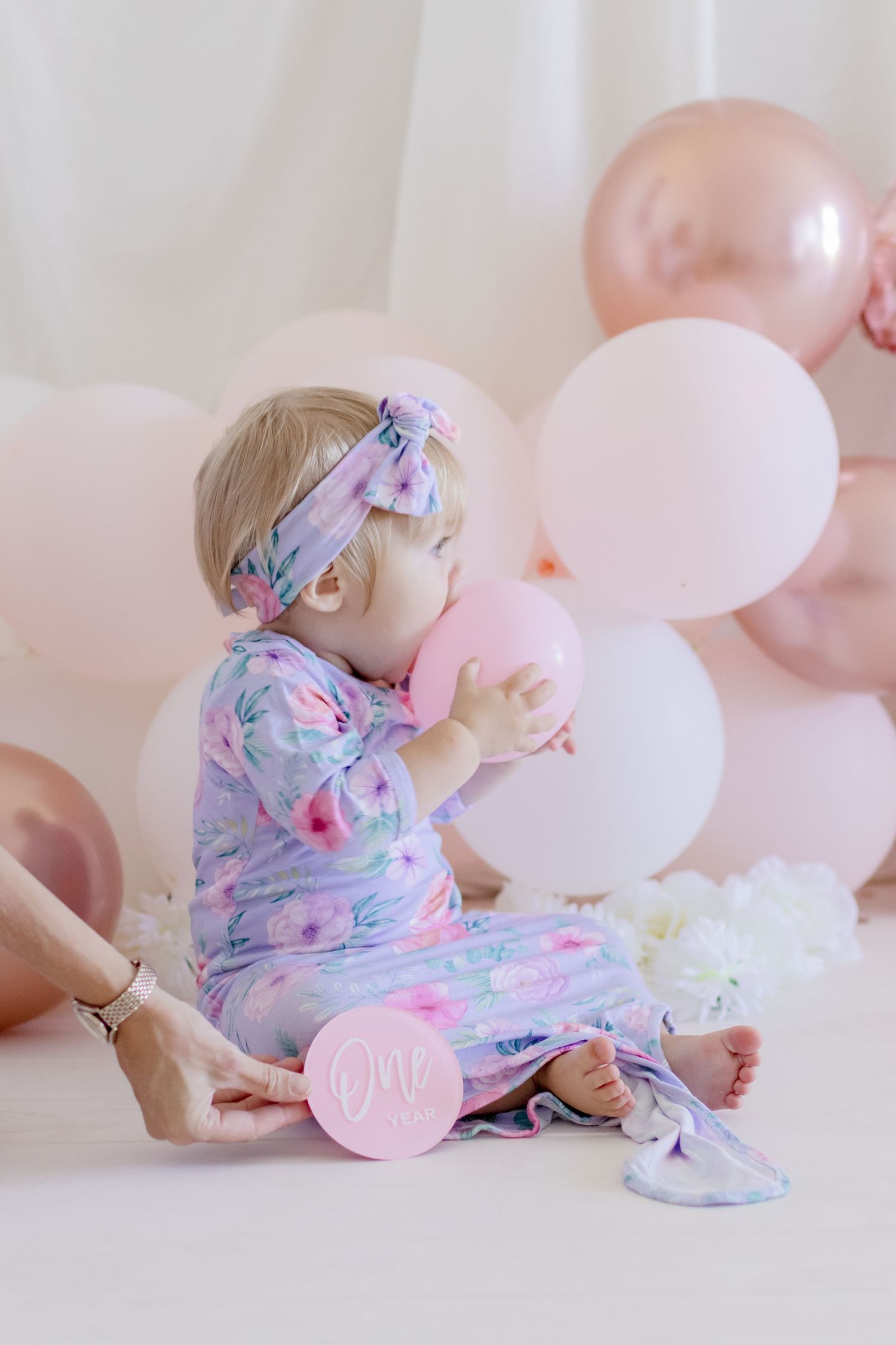 A whimsical pose with balloons wearing a pastel floral outfit in a studio setting.